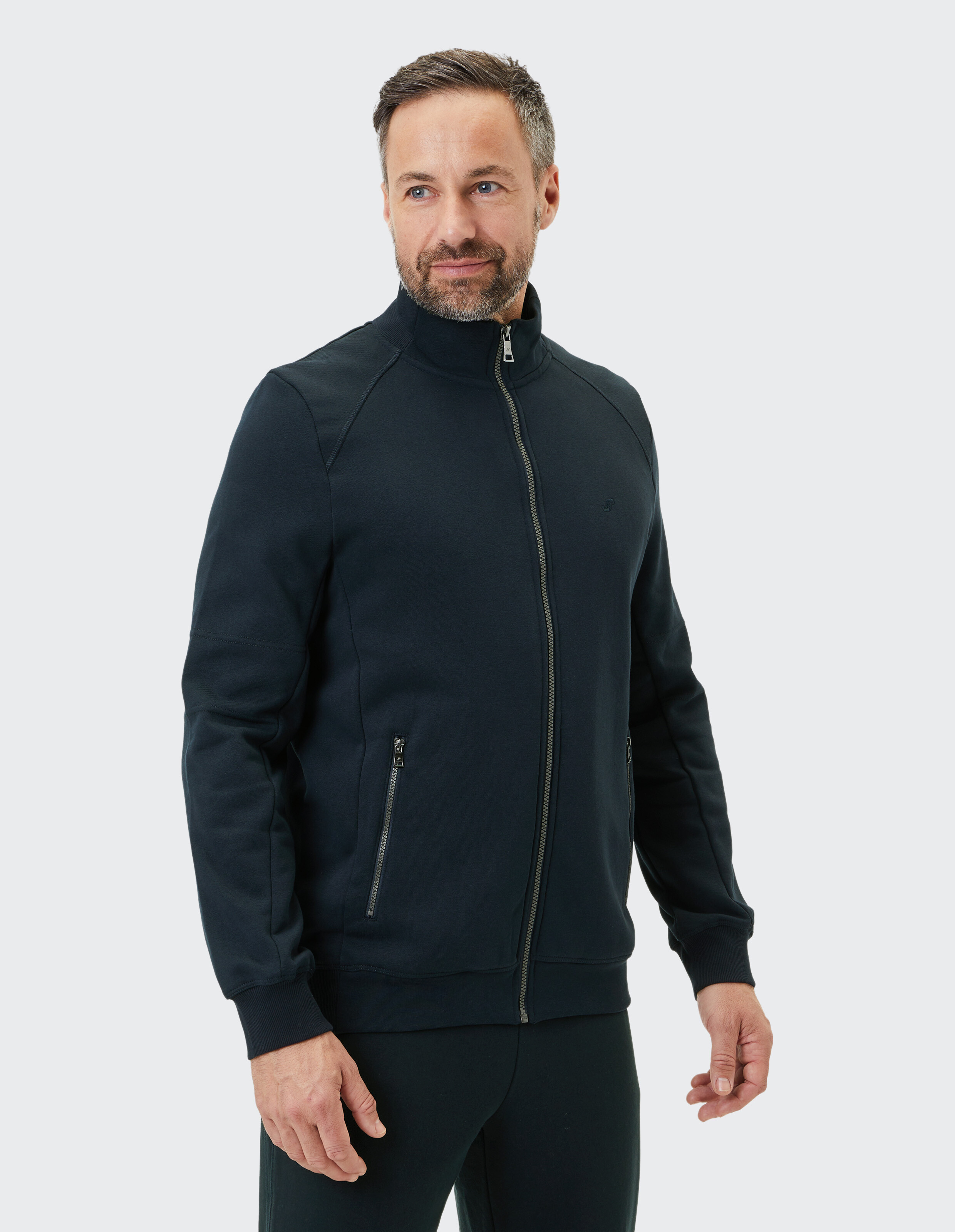 Mann in dunkelblauem Reißverschluss-Pullover mit Stehkragen und seitlichen Reißverschlusstaschen vor hellem Hintergrund.