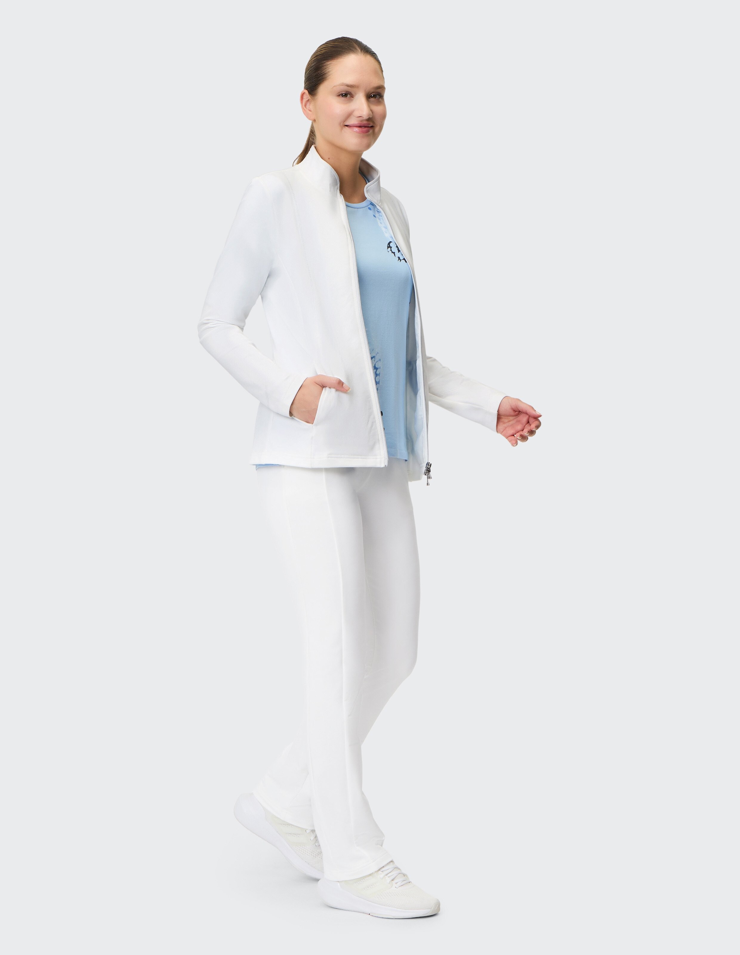 Frau in weißer Jacke und Hose, gepaart mit einem hellblauen Oberteil, zeigt lässigen Stil.