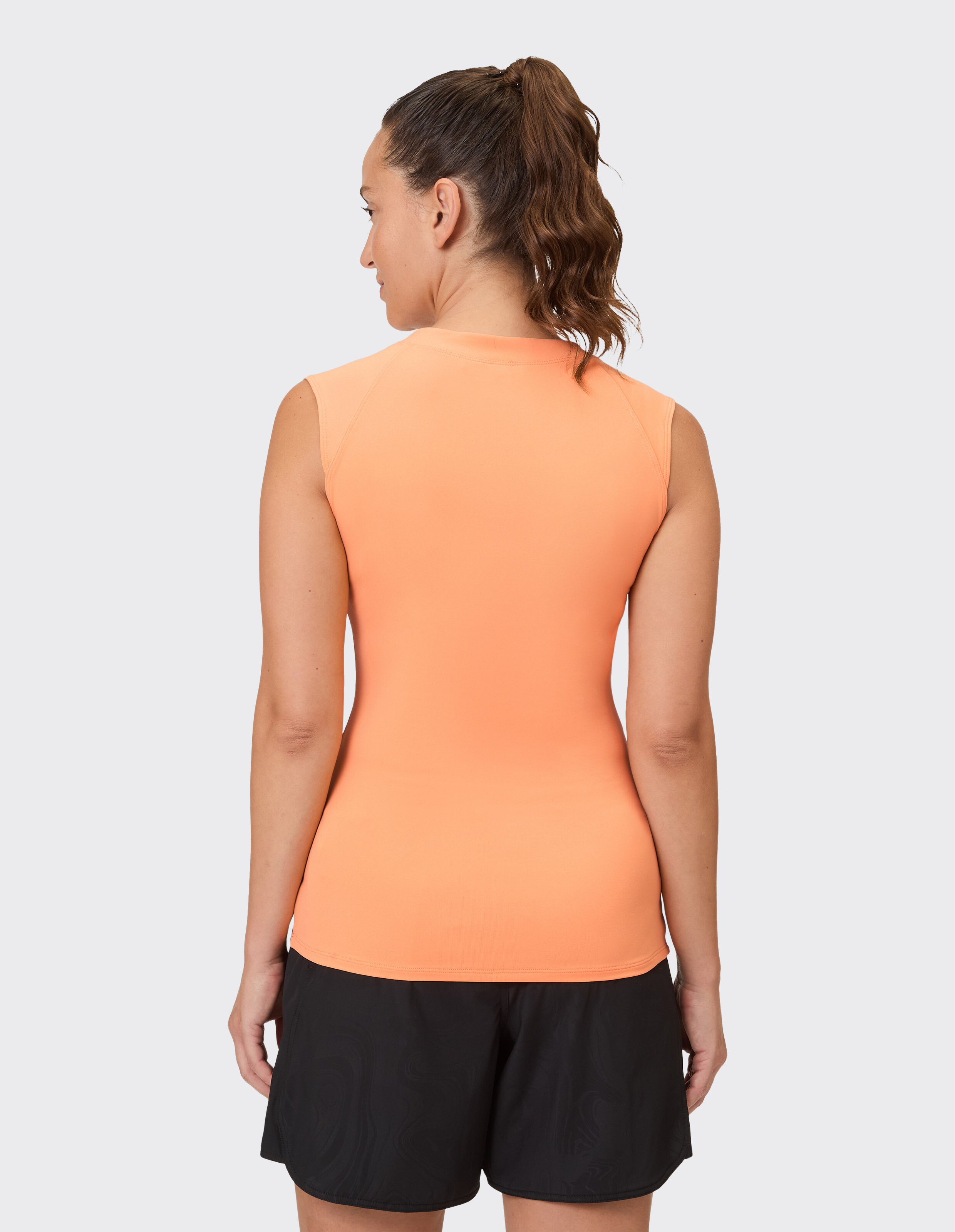 Frau trägt ein ärmelloses orangefarbenes Top und schwarze Shorts für einen lässigen Sommerstil.