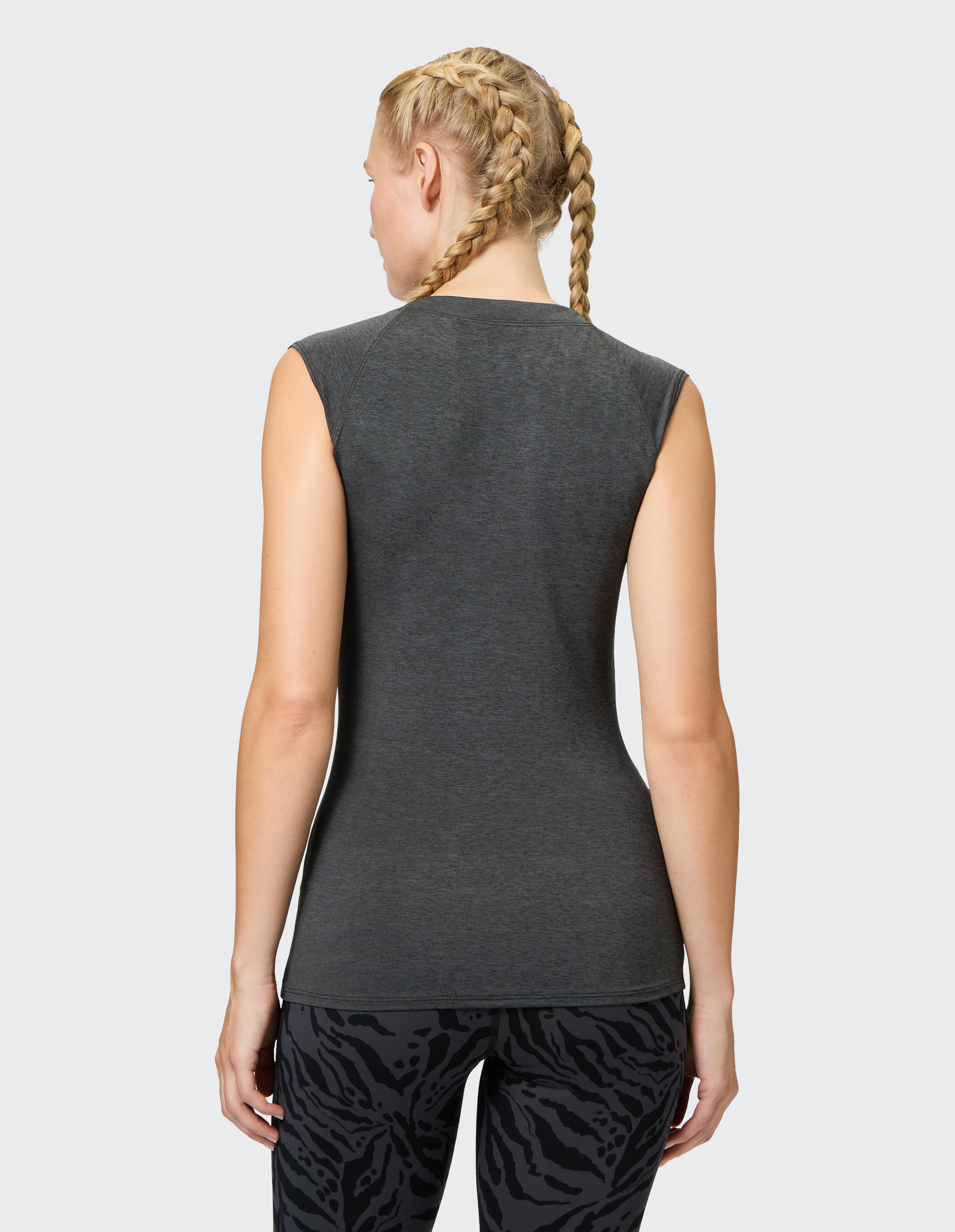 Rückansicht einer Frau in einem enganliegenden grauen ärmellosen Oberteil und gemusterten Leggings.