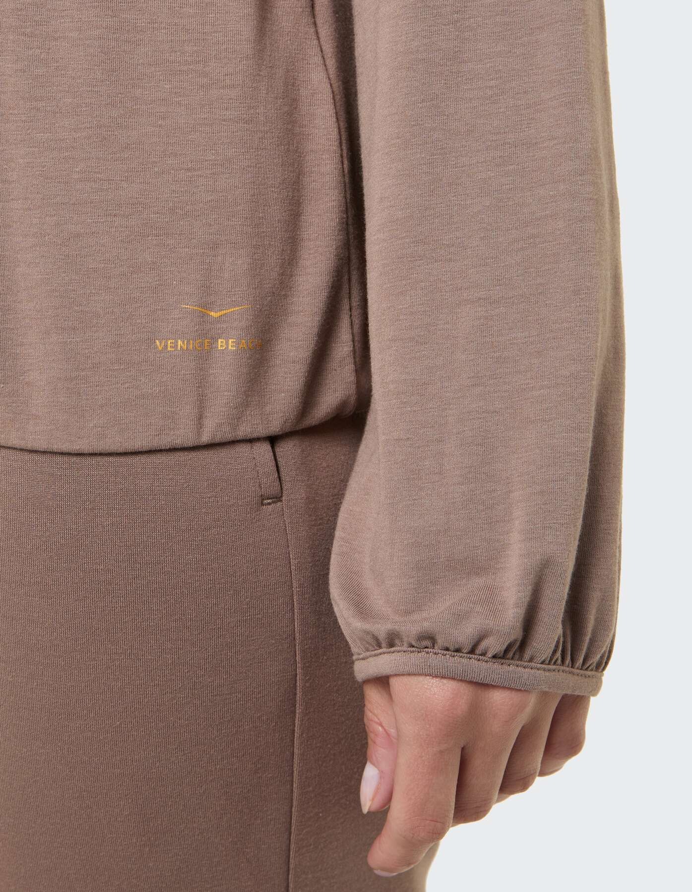 Nahaufnahme eines weichen braunen Langarmoberteils mit elastischen Bündchen und Logodetail.