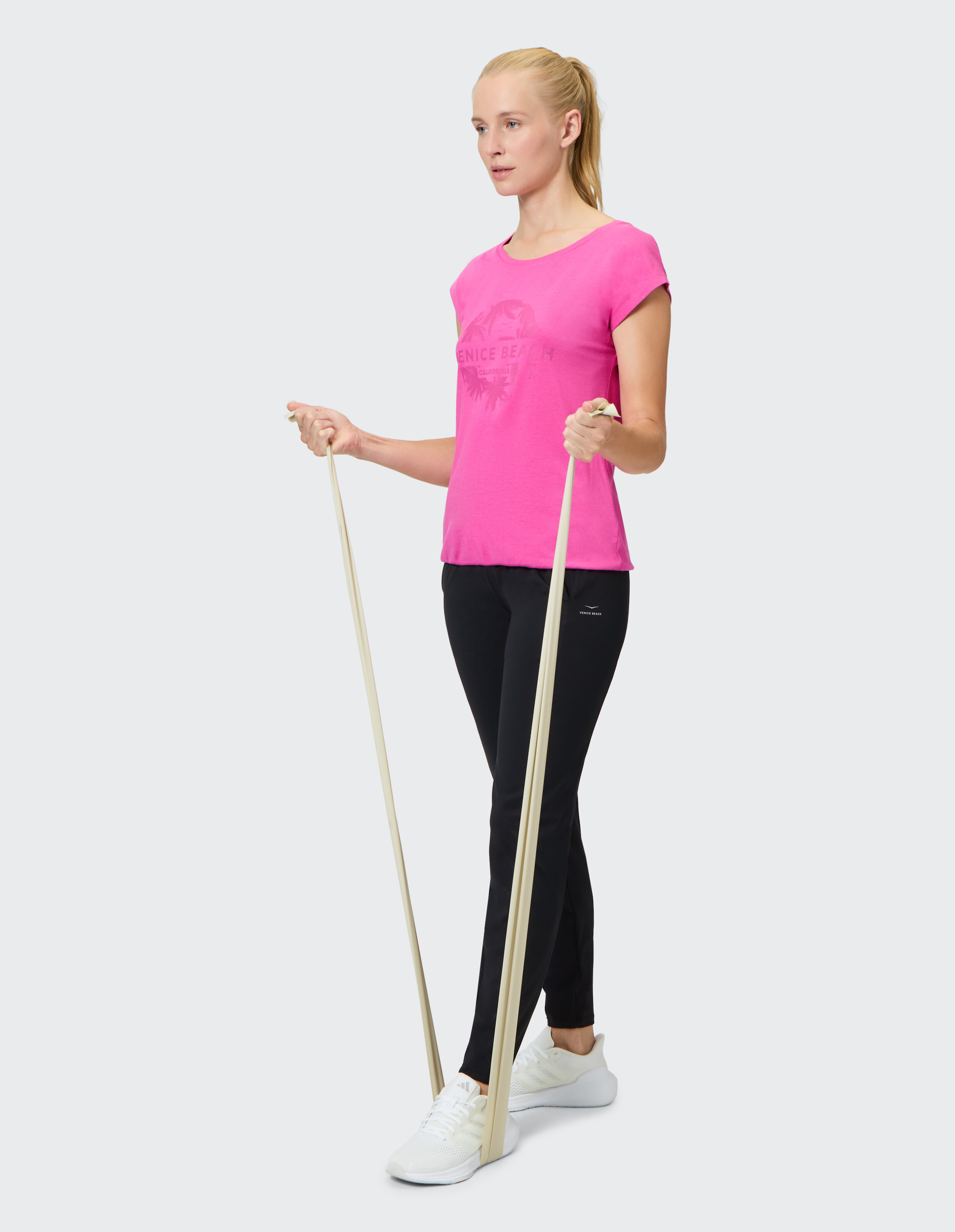 Frau in rosa T-Shirt und schwarzen Leggings trainiert mit Widerstandsbändern.