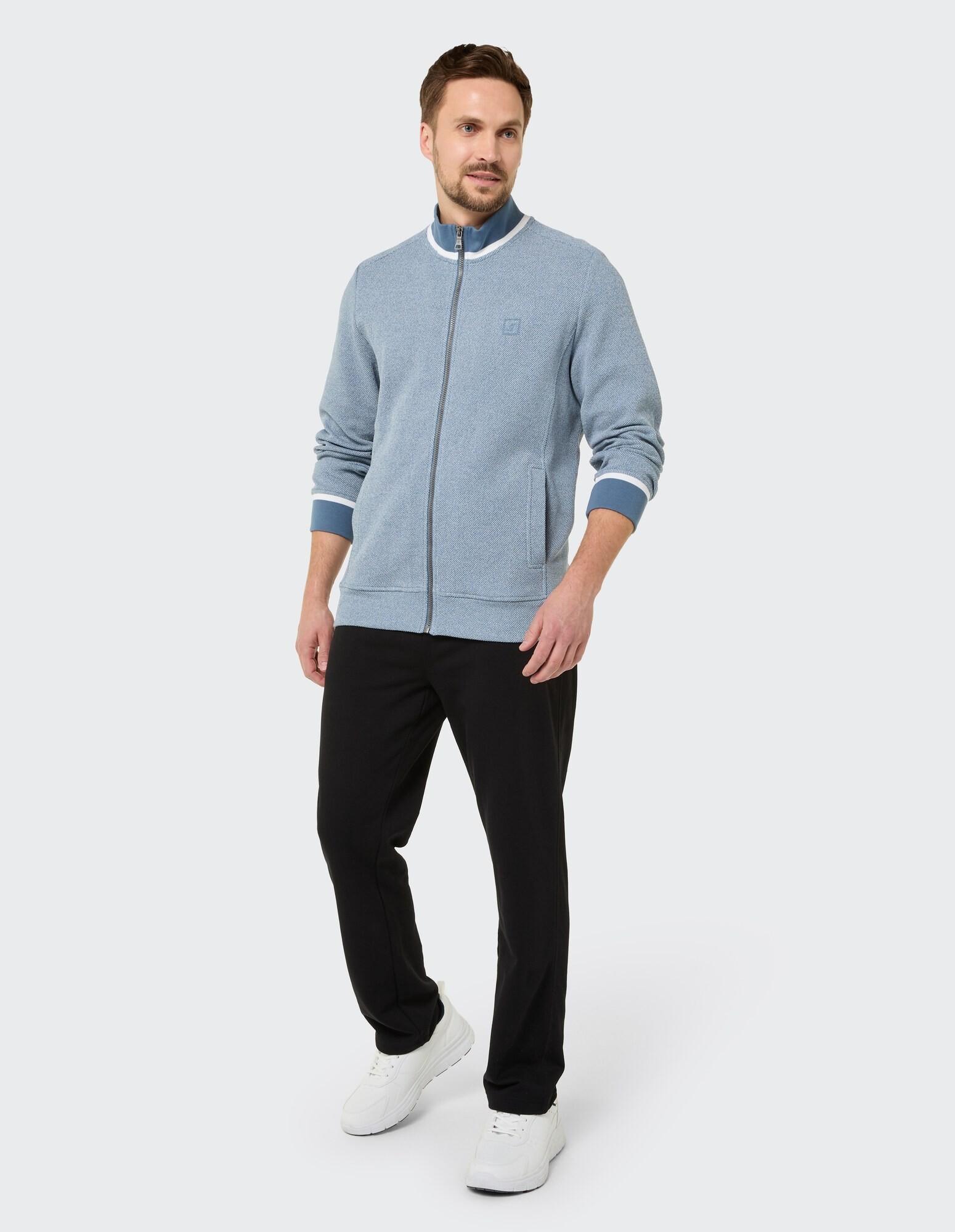 Mann in einer hellblauen Jacke mit Reißverschluss und einer schwarzen Hose, der lässigen Stil zeigt.