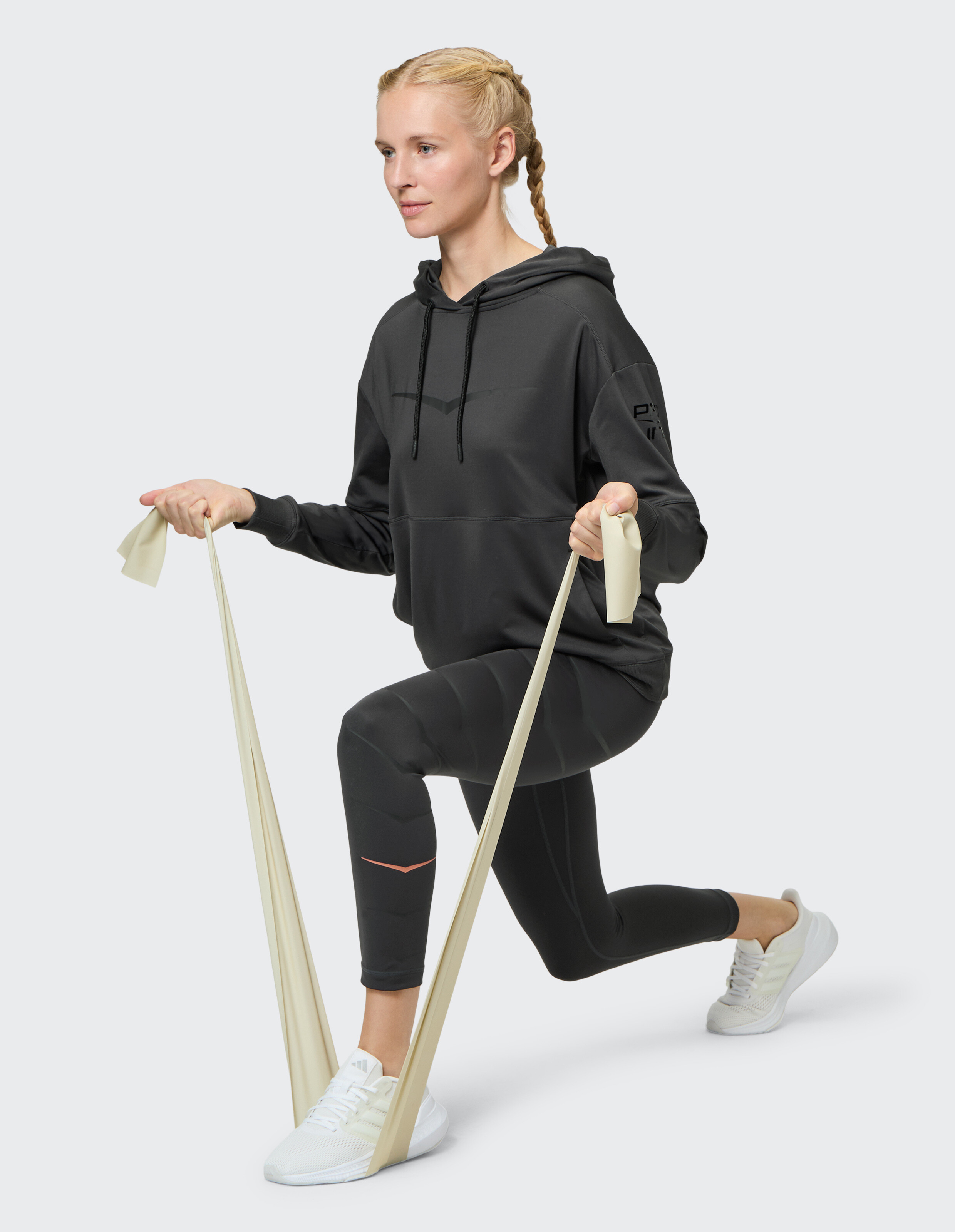 Frau in schwarzem Kapuzenpullover und Leggings trainiert mit Widerstandsbändern.
