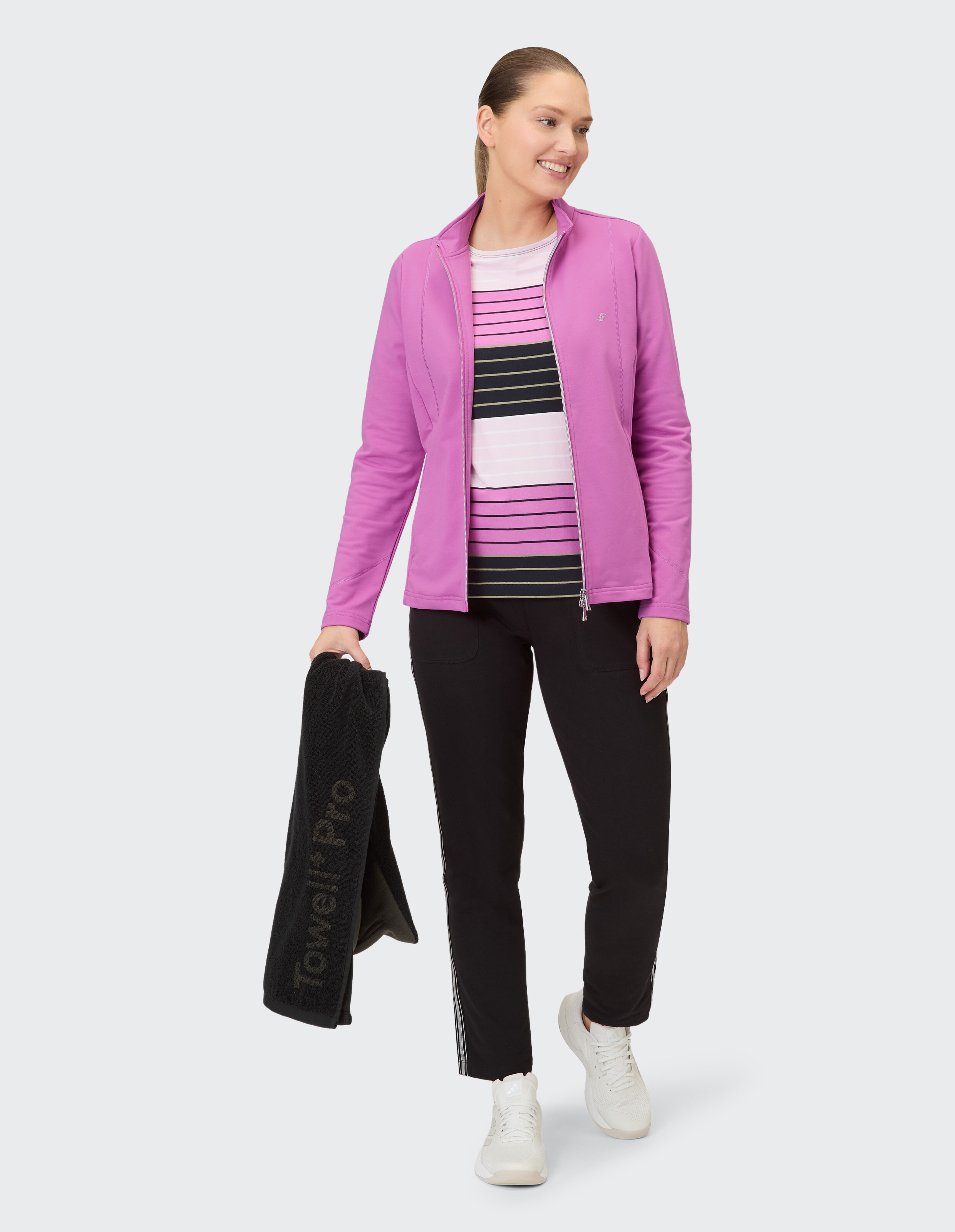 Frau in rosa Jacke und gestreiftem Oberteil, mit einem Handtuch in der Hand, gestylt für Freizeitkleidung.
