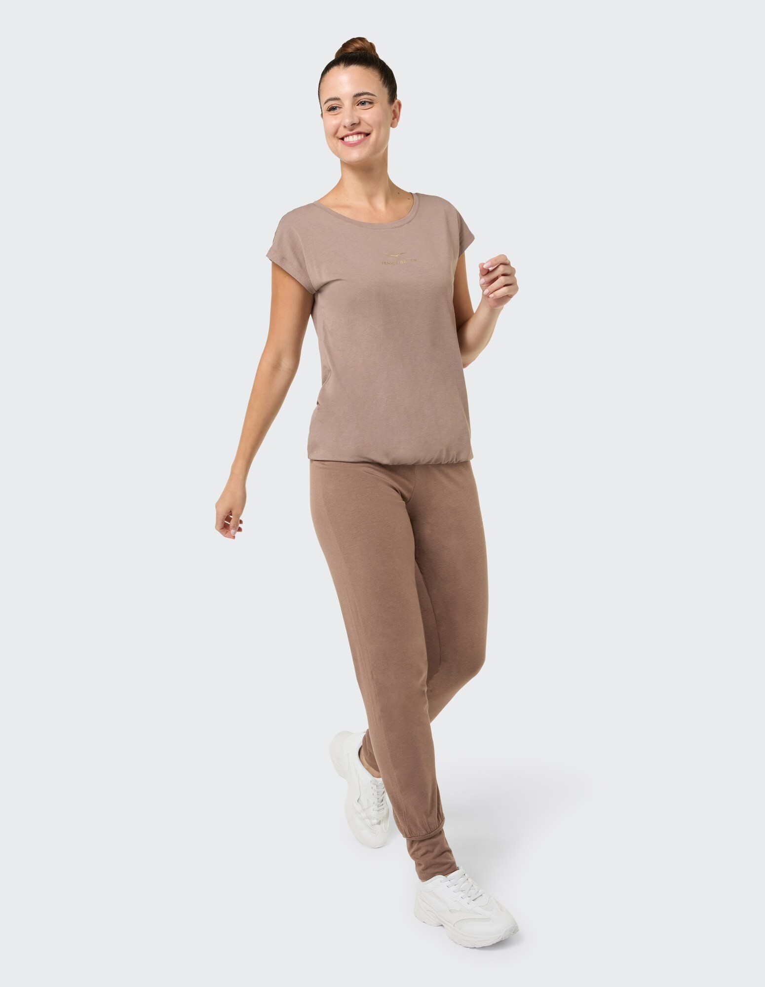 Lächelnde Frau in braunem Freizeit-Top und Leggings, perfekt zum Faulenzen.