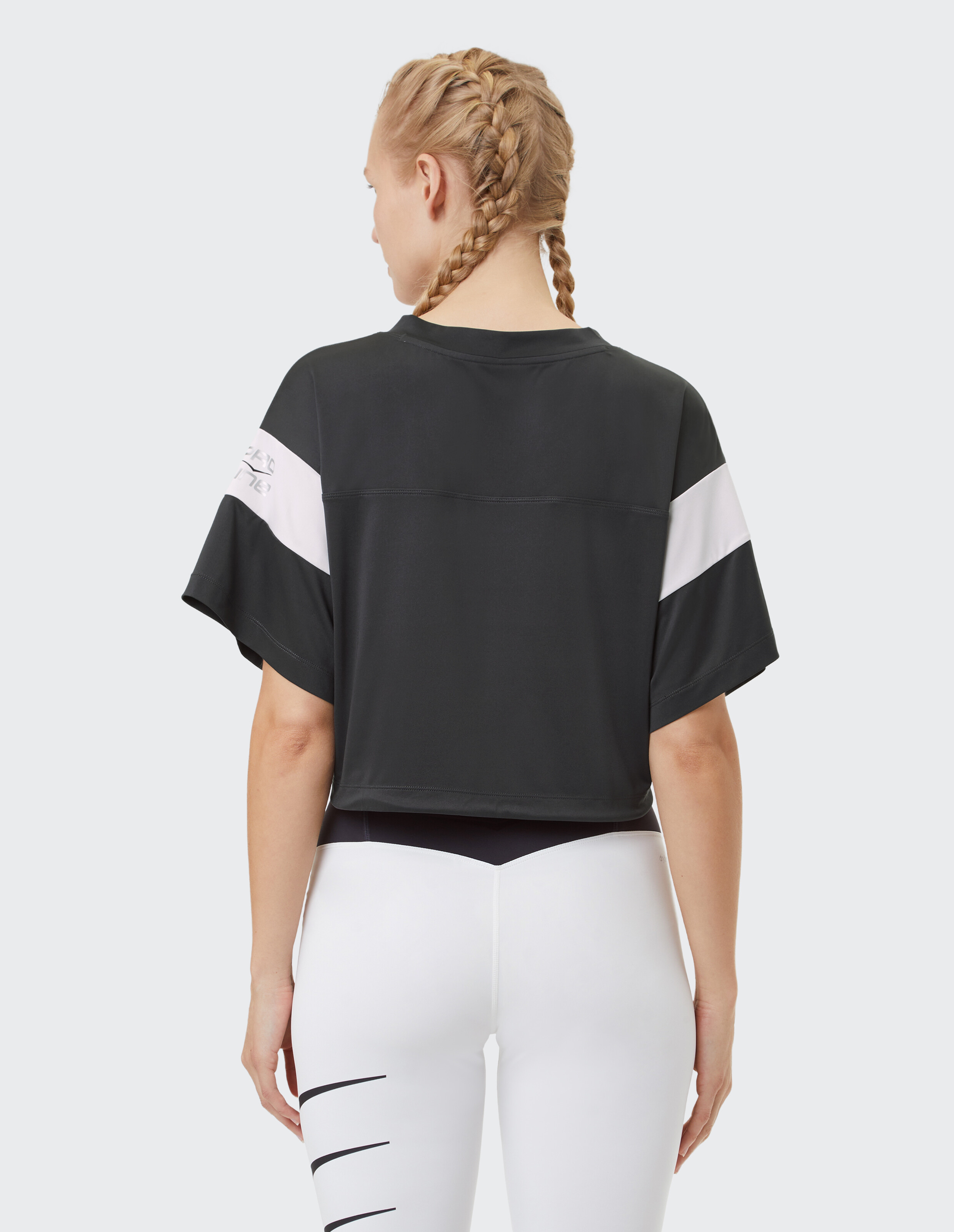 Frau trägt ein schwarzes, kurzes T-Shirt mit weißen Streifen und weißen Leggings.