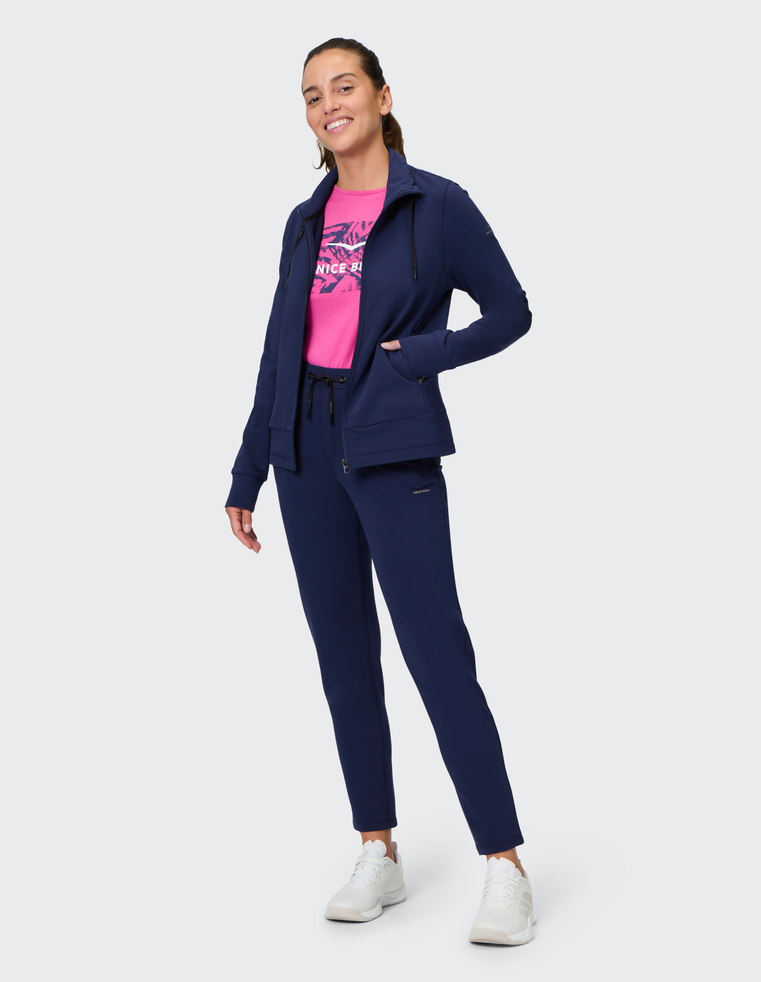 Lächelnde Frau in dunkelblauer Freizeitjacke und Hose mit rosafarbenem Grafik-T-Shirt.