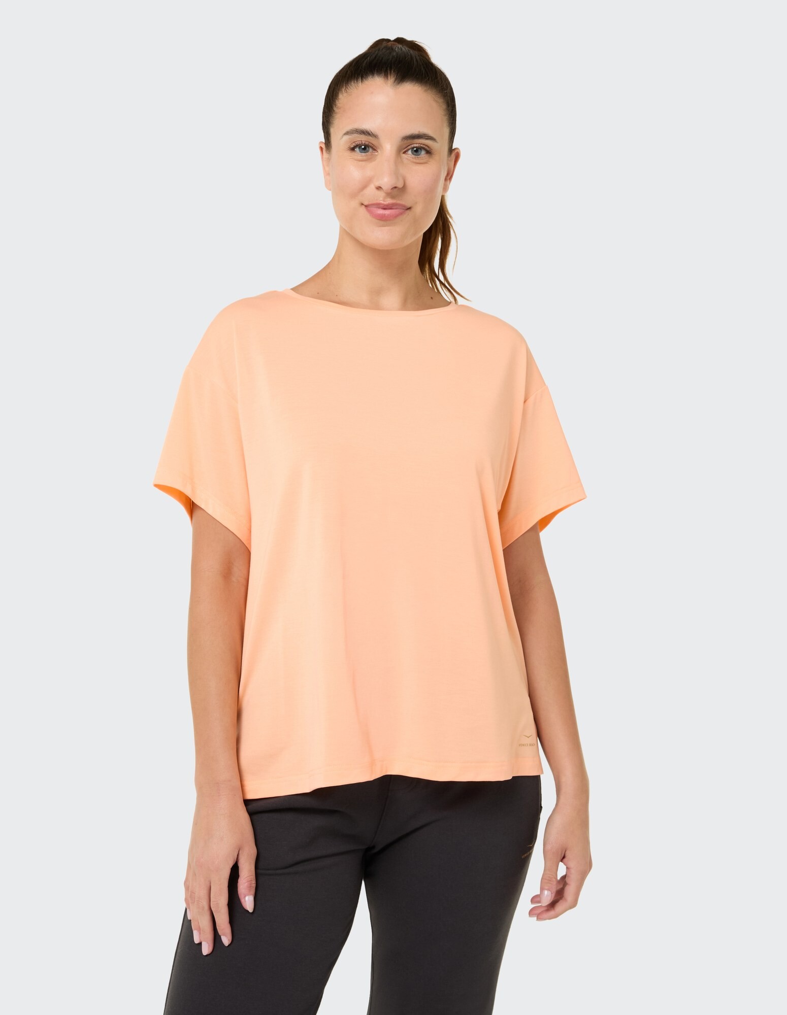Frau trägt ein gemütliches, pfirsichfarbenes, übergroßes T-Shirt mit entspannter Passform und kurzen Ärmeln.