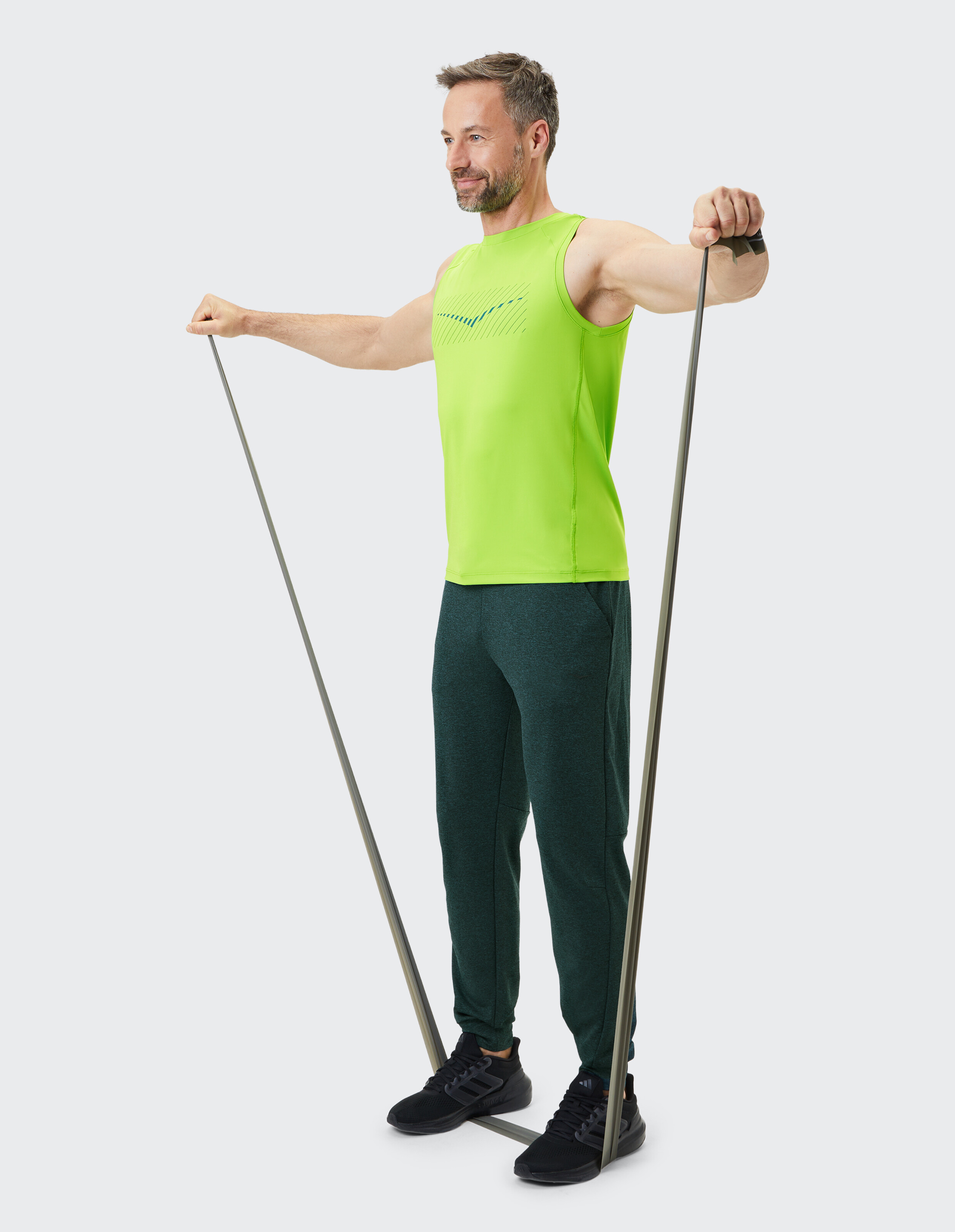 Mann im neongrünen Tanktop und dunkelgrünen Joggern trainiert mit Widerstandsbändern.