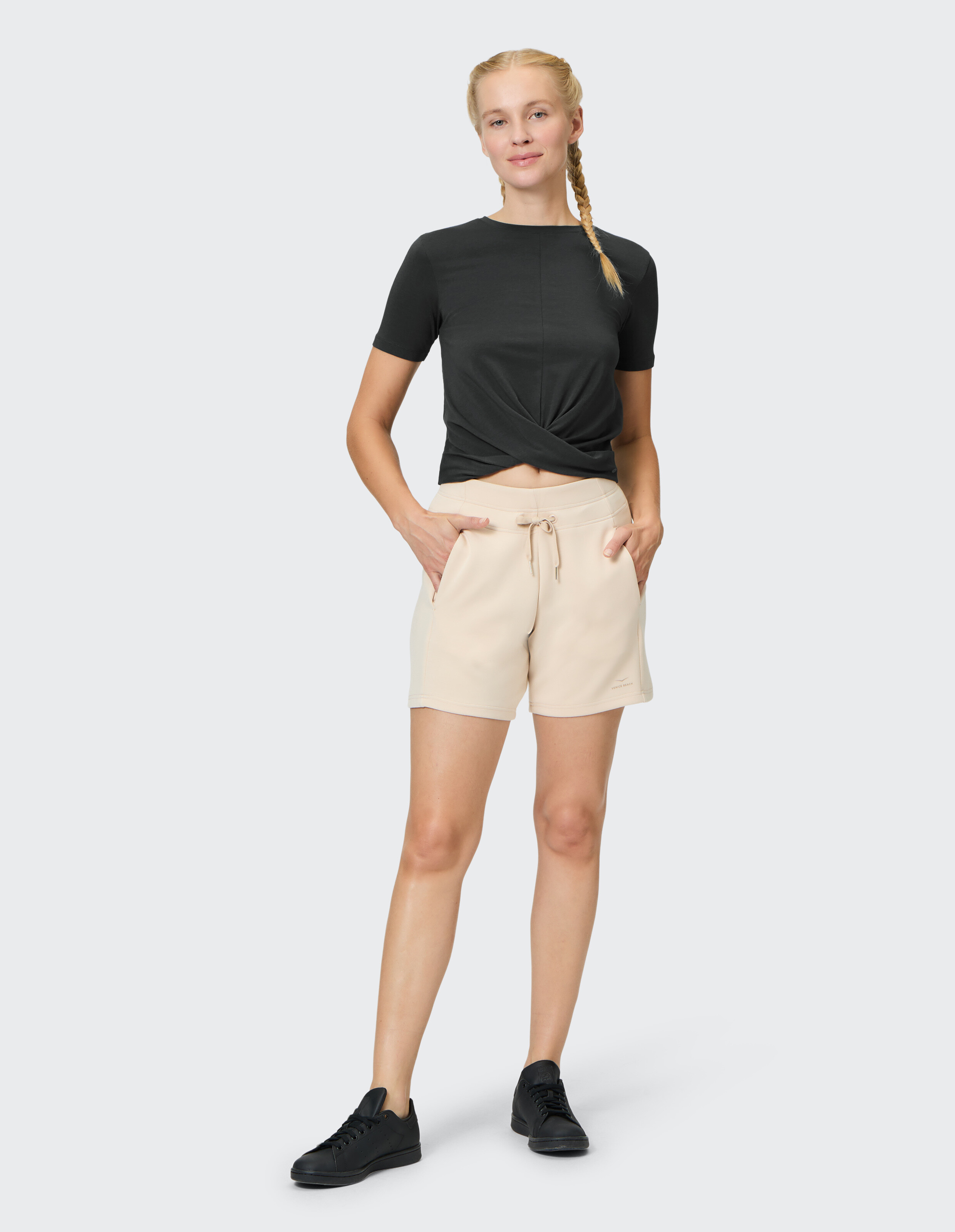 Frau trägt ein schwarzes, kurzärmeliges Venice Beach Darleen-Hemd und beige Shorts.