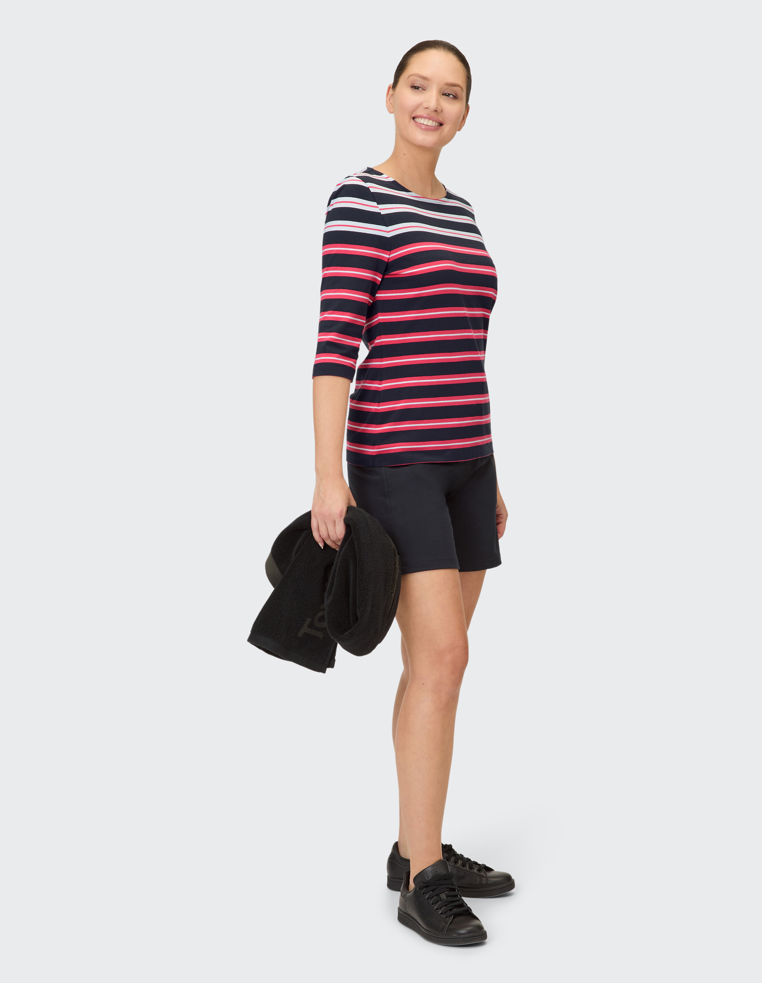 Frau in einem gestreiften Langarmshirt und schwarzen Shorts, hält ein Handtuch in der Hand.