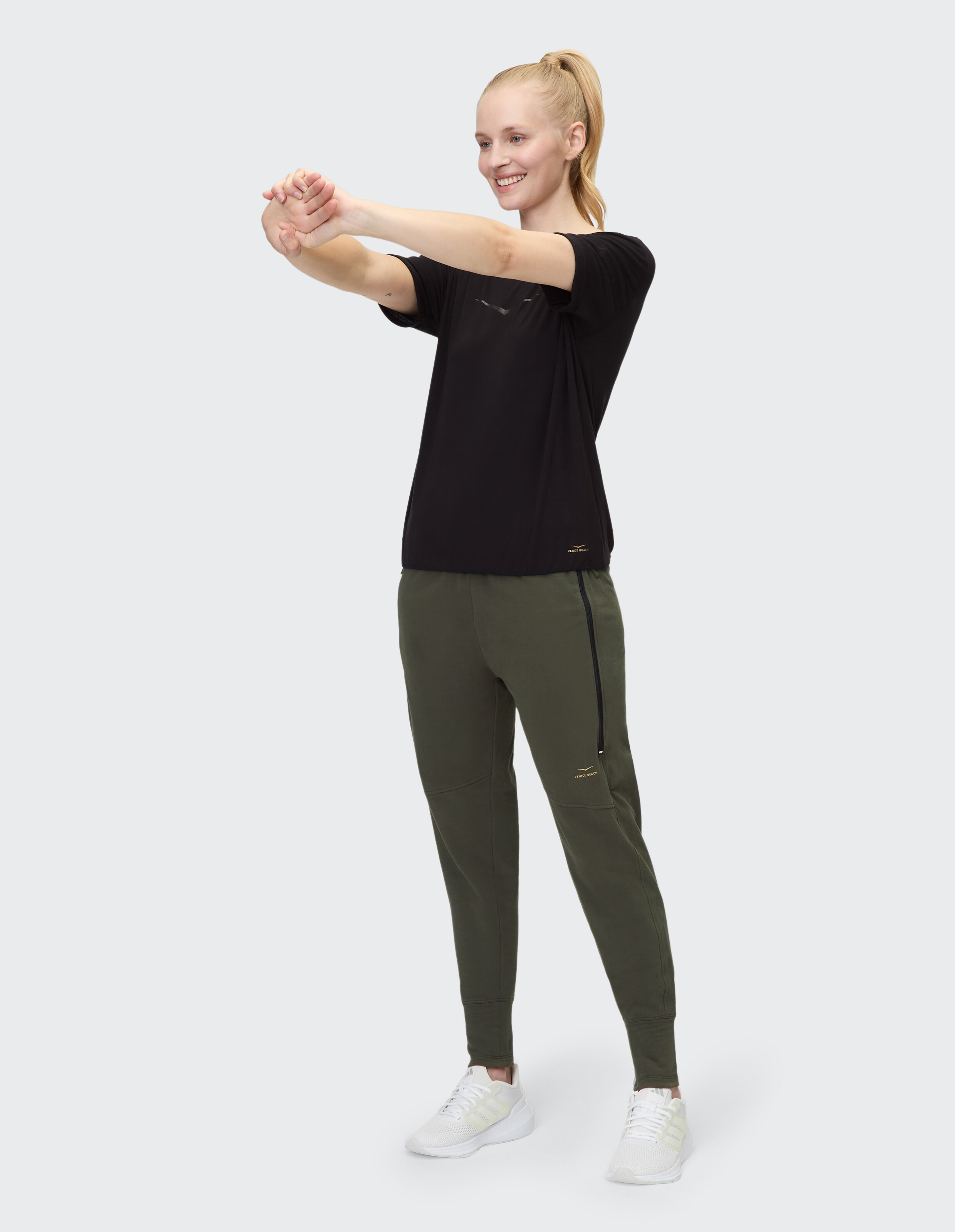 Frau im schwarzen T-Shirt und olivfarbenen Jogginghosen im lässigen Activewear-Stil.