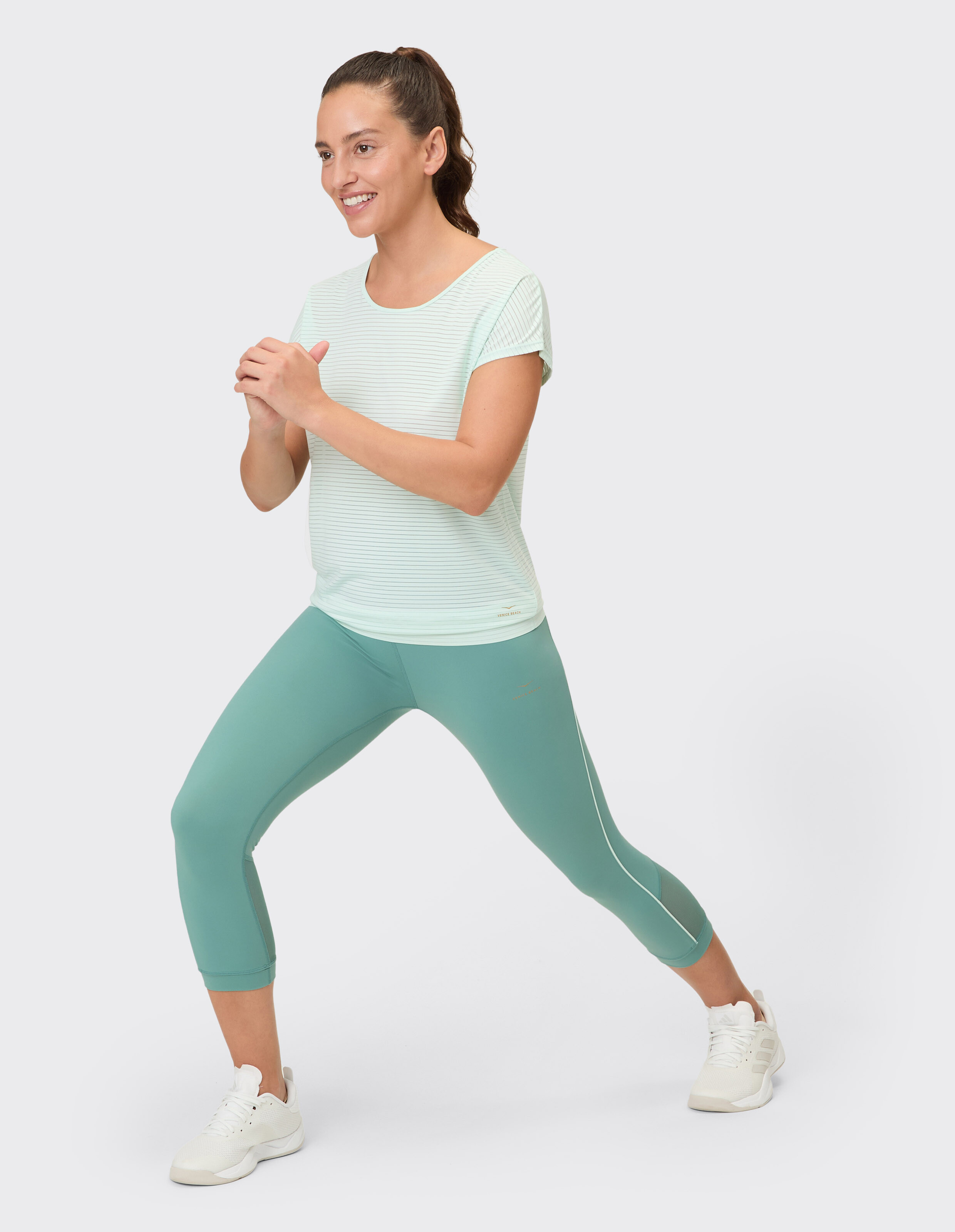 Frau in hellgrünem, gestreiftem Oberteil und blaugrünen Leggings im Activewear-Stil.