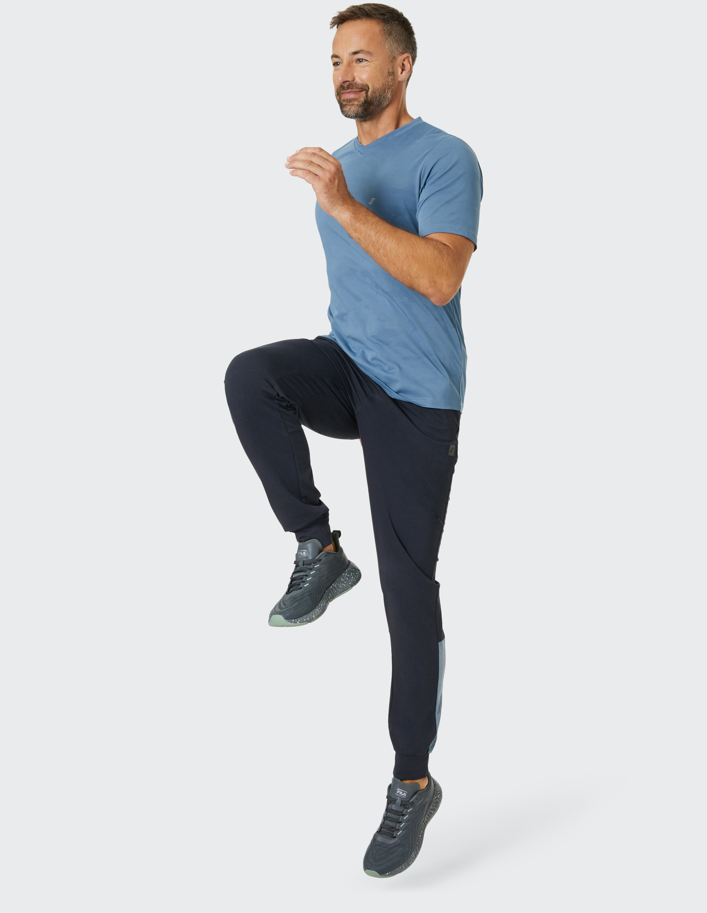 Mann in blauem T-Shirt und dunkelblauen Jogginghosen präsentiert lässige Sportkleidung.
