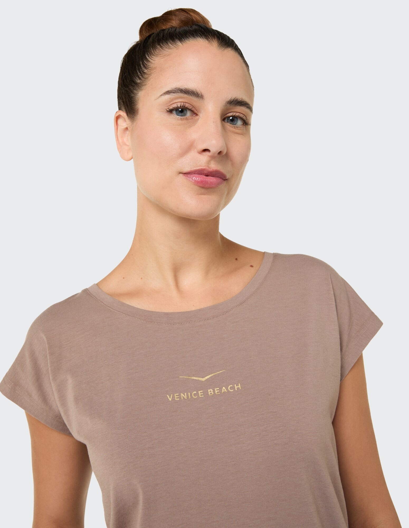 Frau trägt ein hellbraunes T-Shirt mit „VENICE BEACH“-Aufdruck im lässigen Stil.