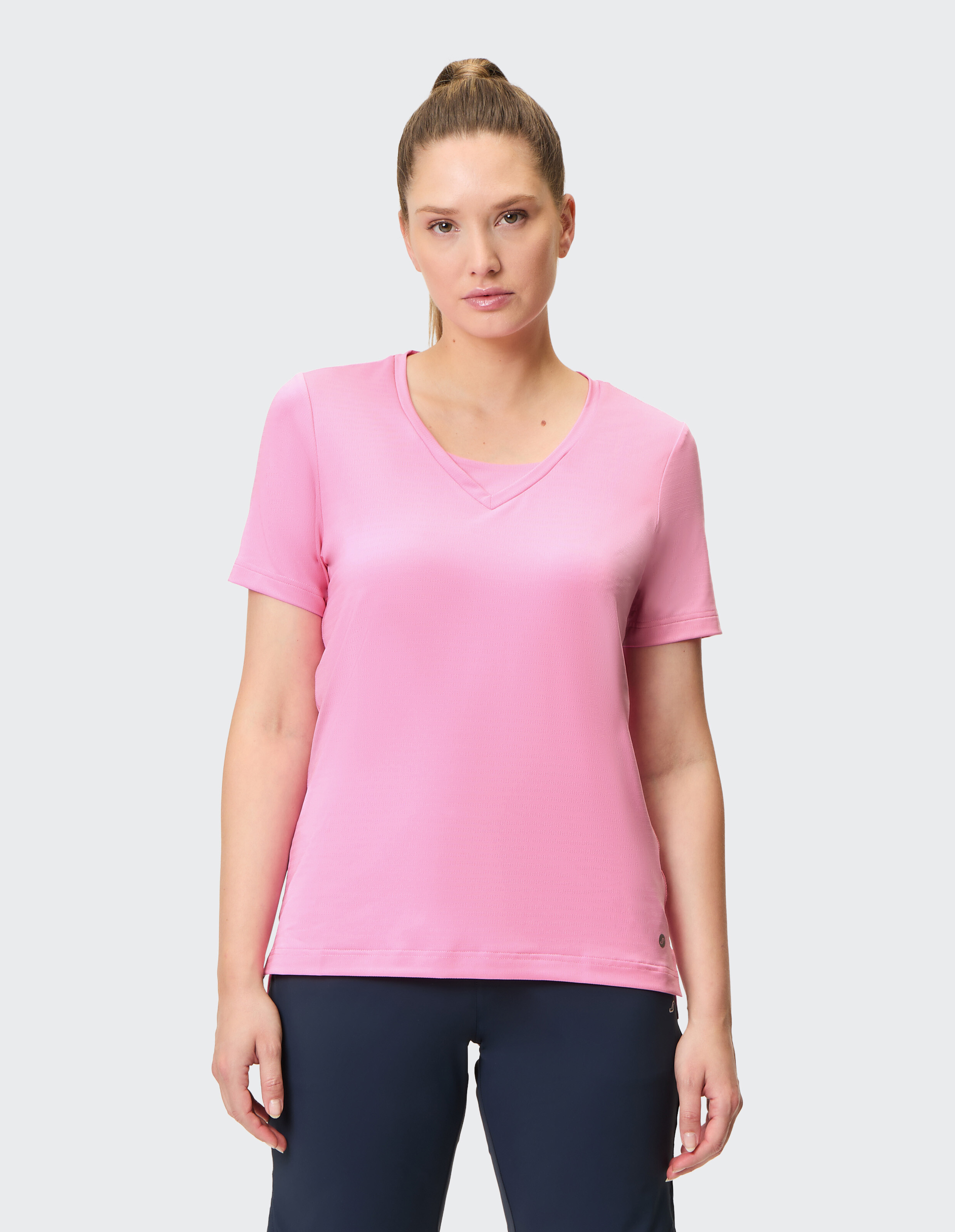 Frau trägt ein rosafarbenes Freizeit-T-Shirt mit V-Ausschnitt und eine dunkle Hose für einen bequemen Look.