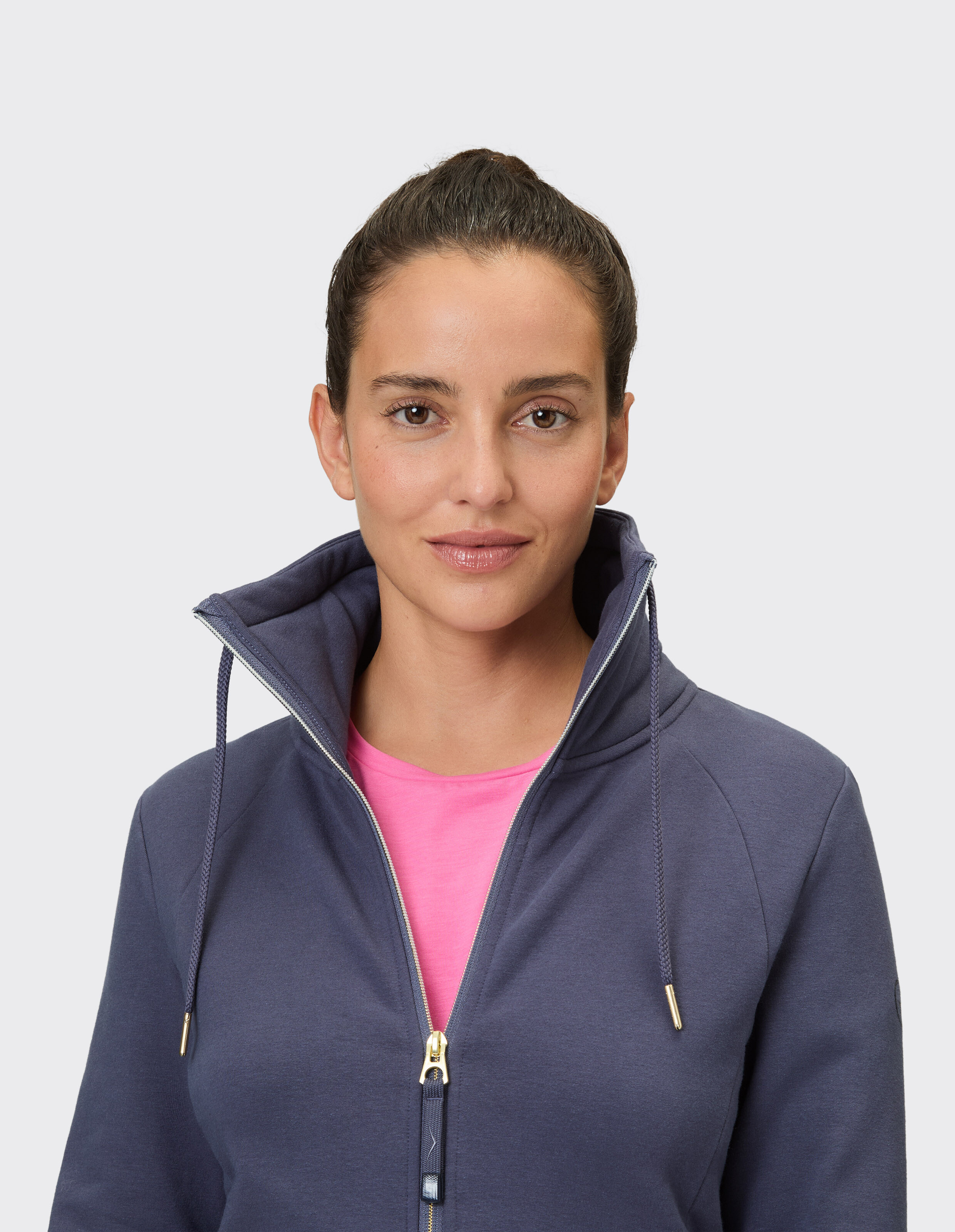 Frau in einem dunkelblauen Kapuzenpullover mit Reißverschluss über einem rosa Hemd, das lässigen Stil unterstreicht.
