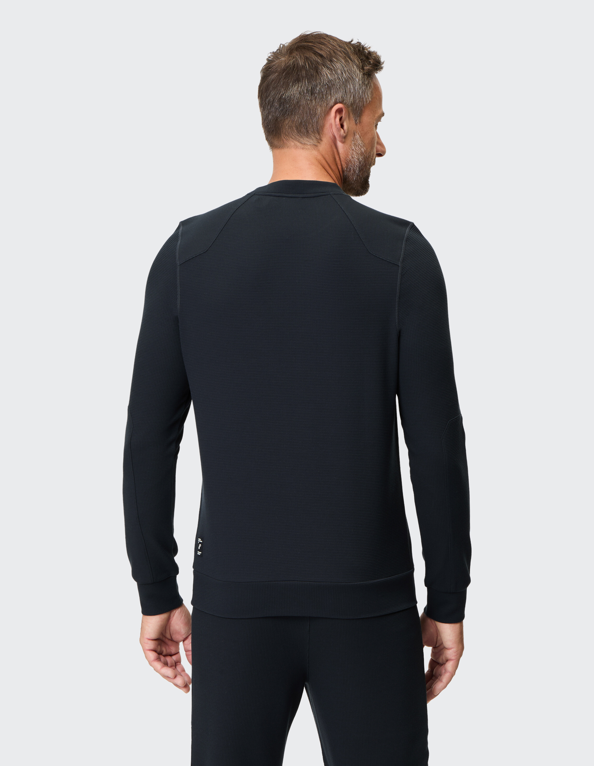 Rückansicht eines Mannes, der ein schwarzes, strukturiertes Freizeit-Sweatshirt trägt.