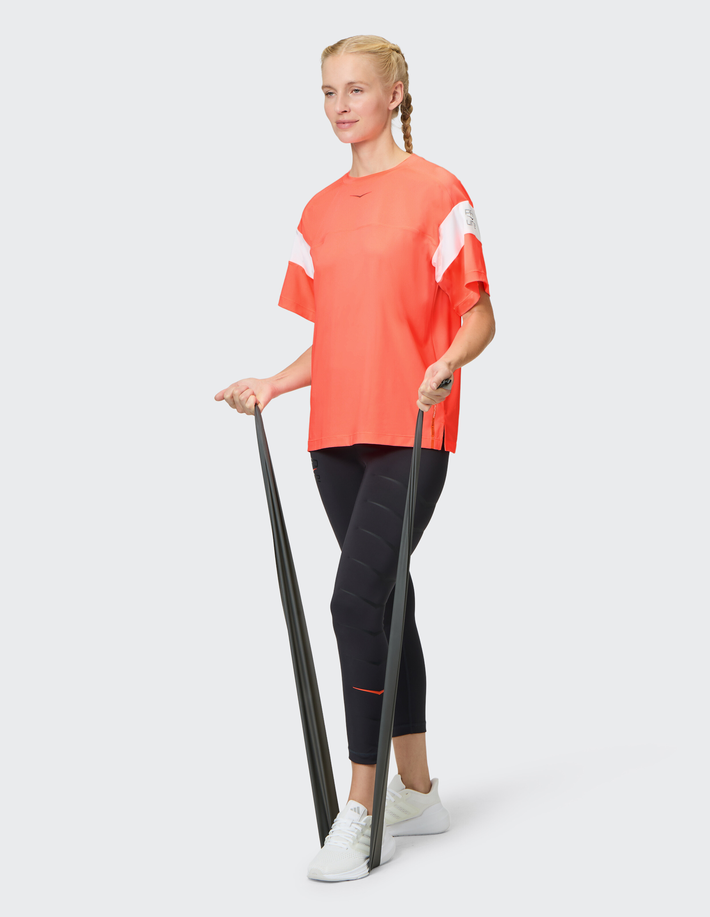 Frau in orangefarbenem T-Shirt und schwarzen Leggings trainiert mit einem Widerstandsband.