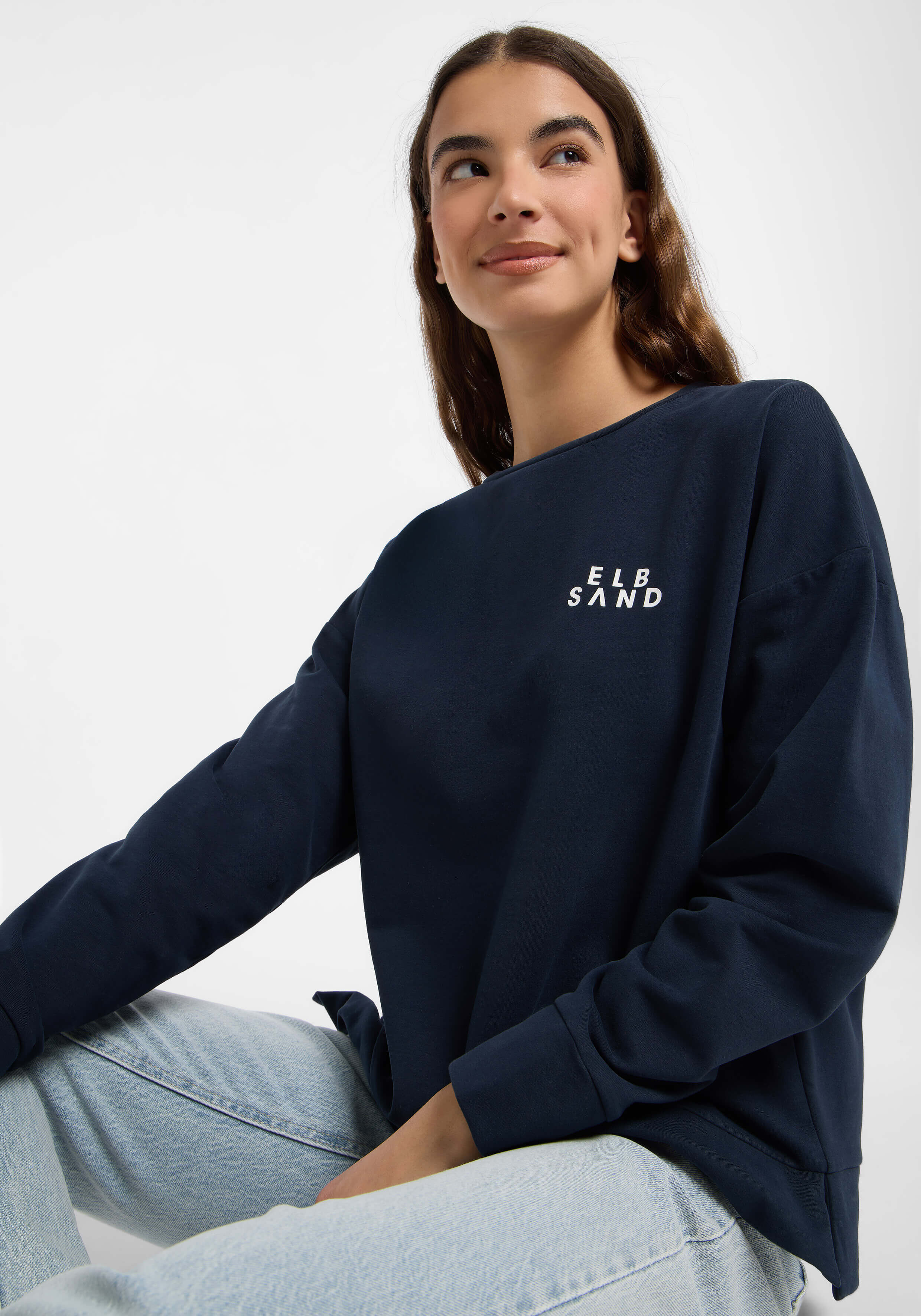 Frau trägt ein dunkelblaues ELBSAND-Sweatshirt mit weißem Logo, gepaart mit hellblauen Jeans.