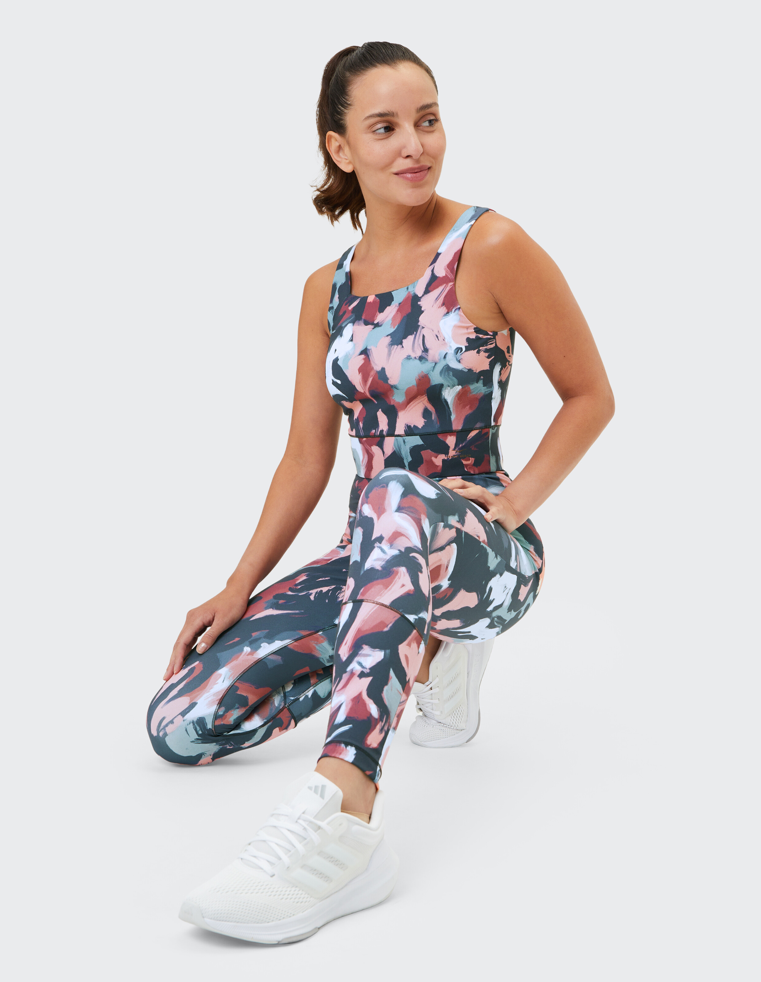 Frau trägt ein farbenfrohes Activewear-Set mit abstraktem Print, Leggings und Tanktop.