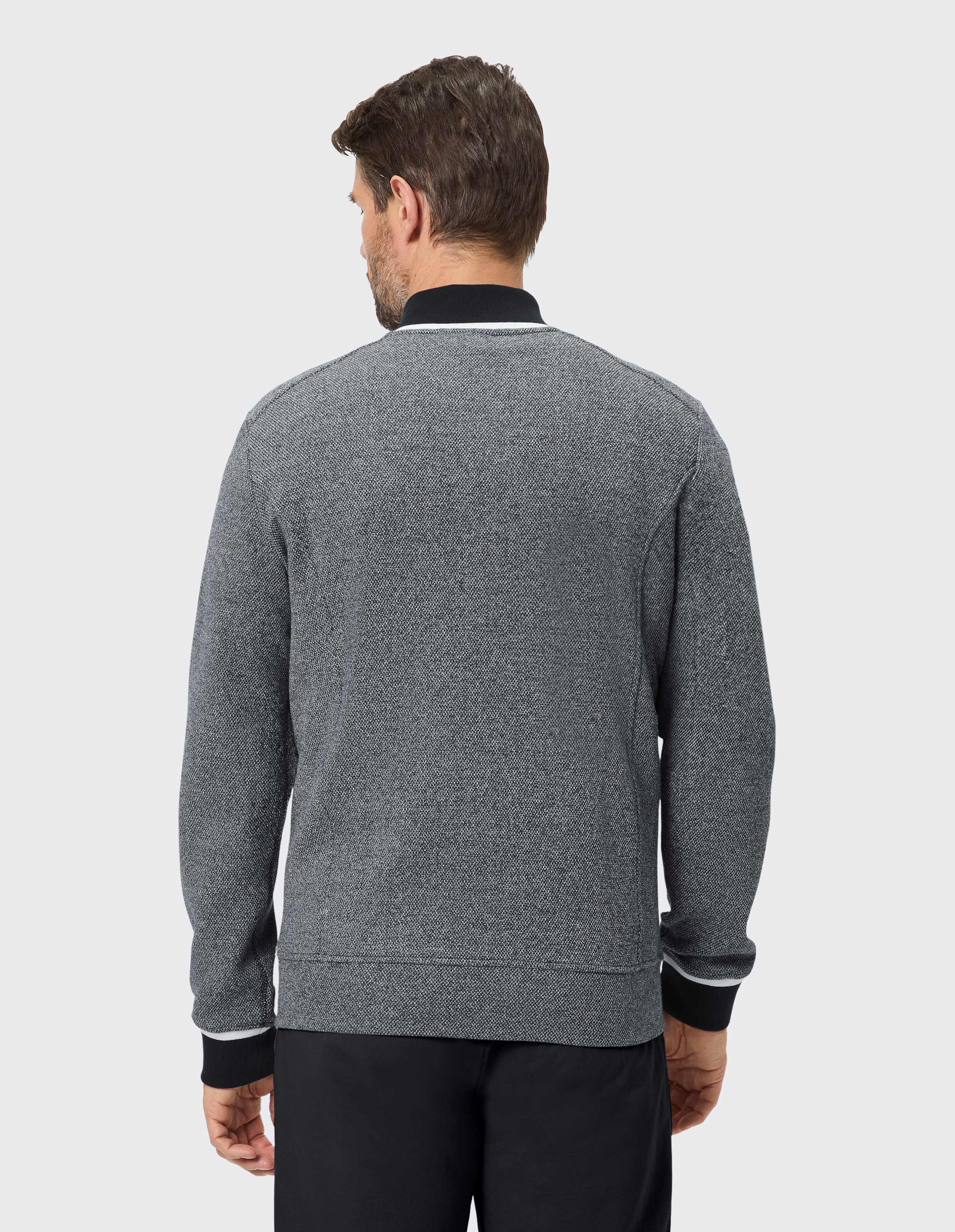 Ein Mann trägt einen melierten grauen Pullover mit weiß-schwarzem Kragen und Ärmelbündchen.