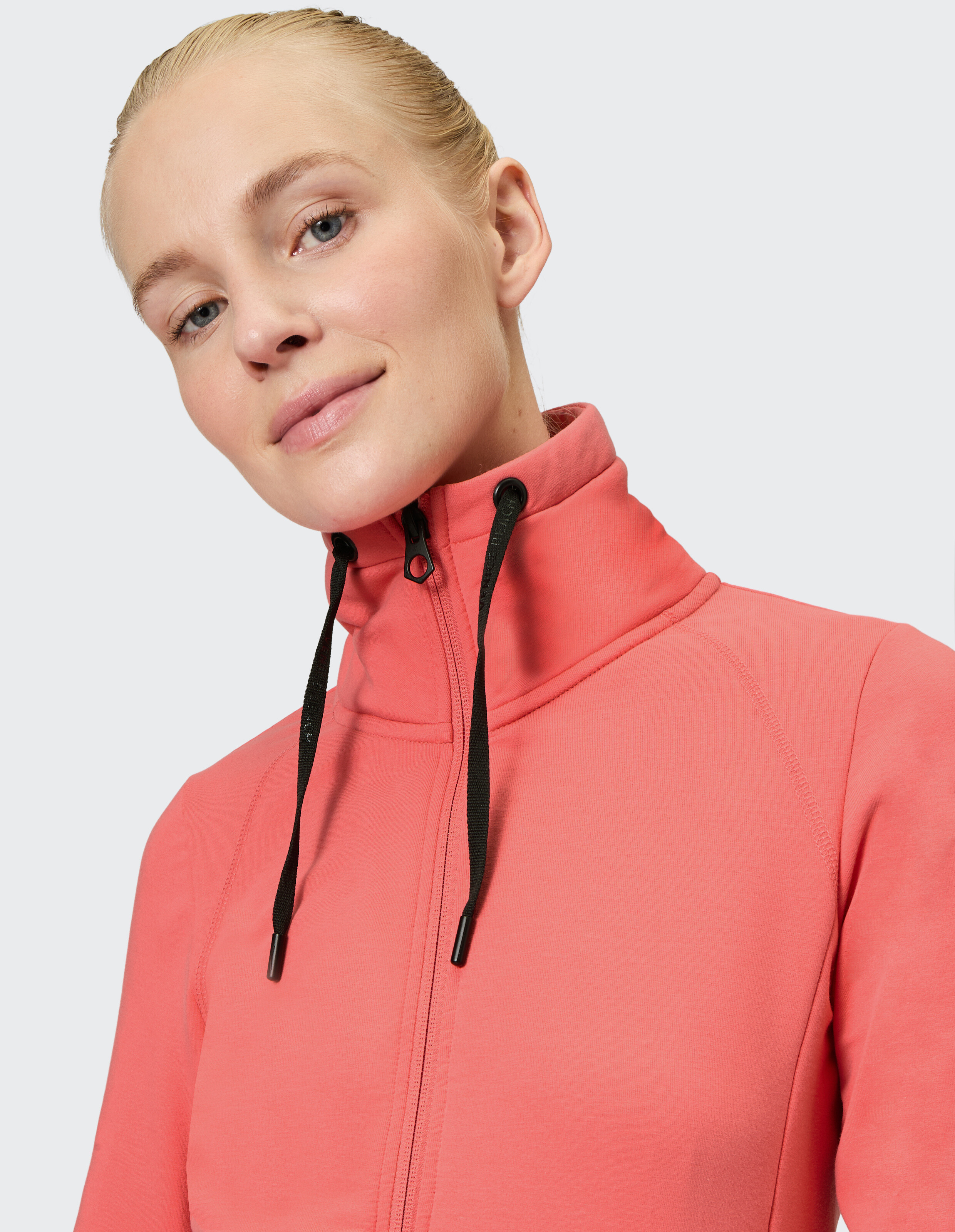 Frau trägt eine korallenrote Venice Beach Florence Sweatjacke mit hohem Kragen.