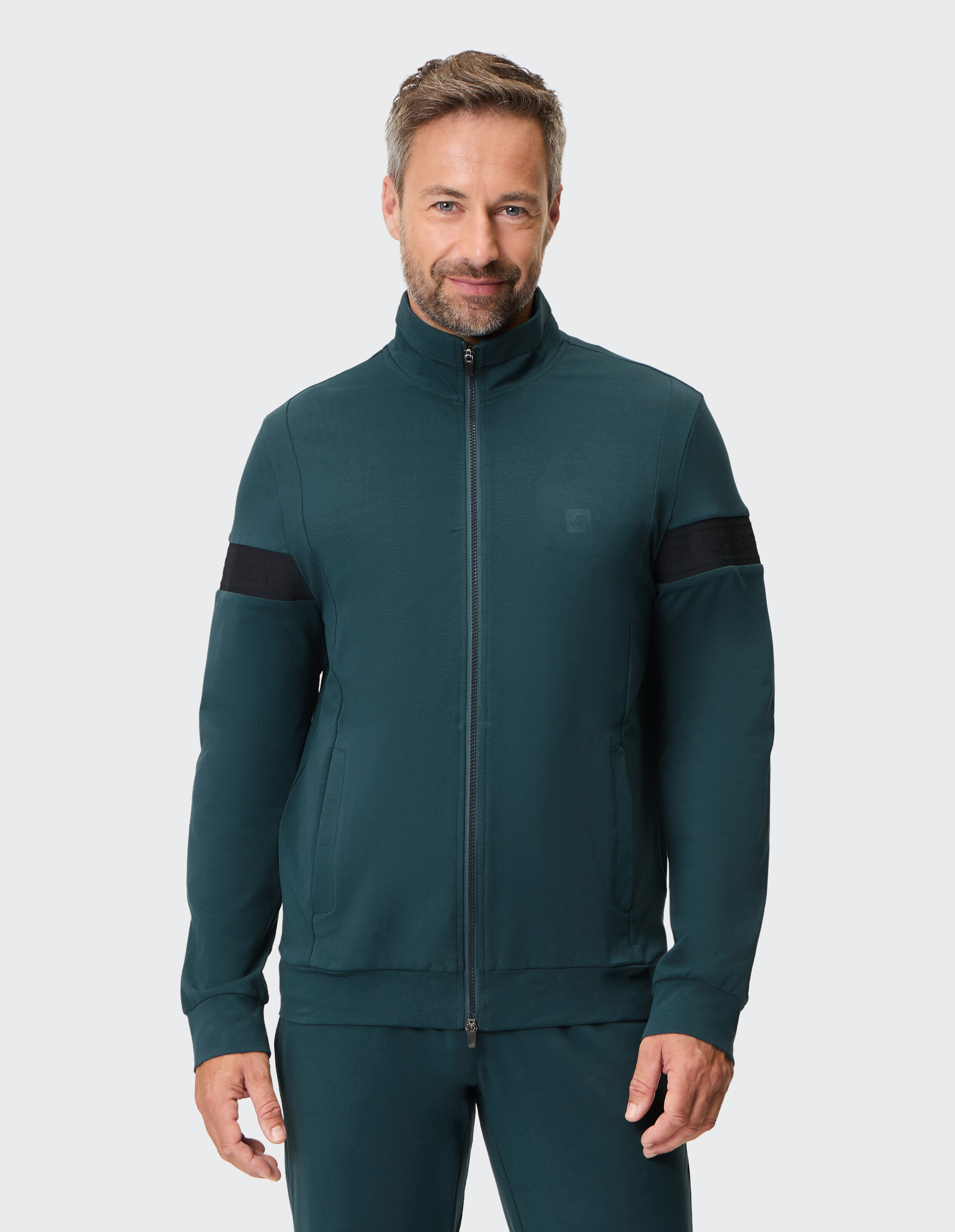Mann trägt eine dunkelgrüne Freizeit-Trainingsjacke mit Reißverschluss und schwarzen Ärmeldetails.
