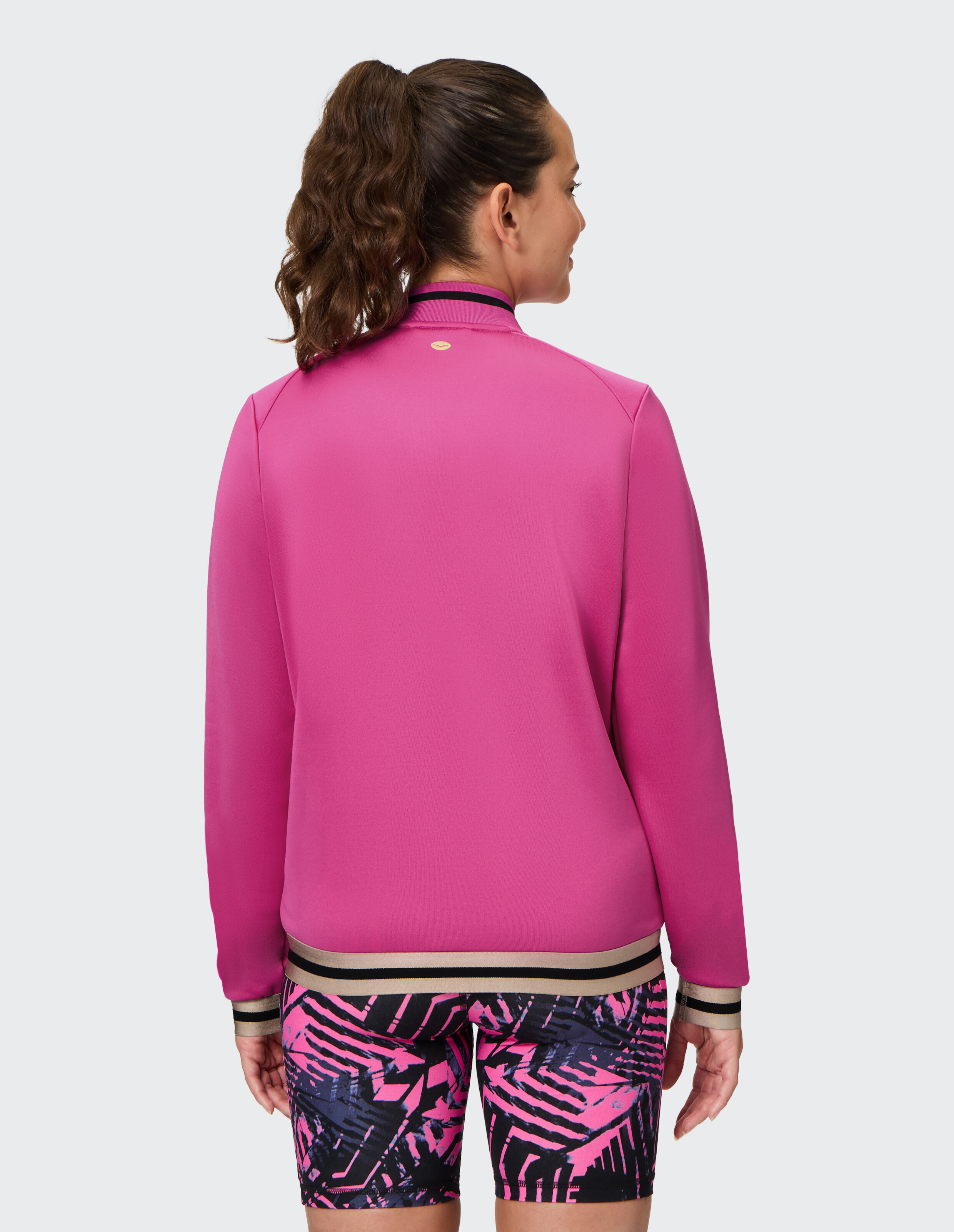 Rückansicht einer Frau in einer rosa Jacke gepaart mit gemusterten Shorts.