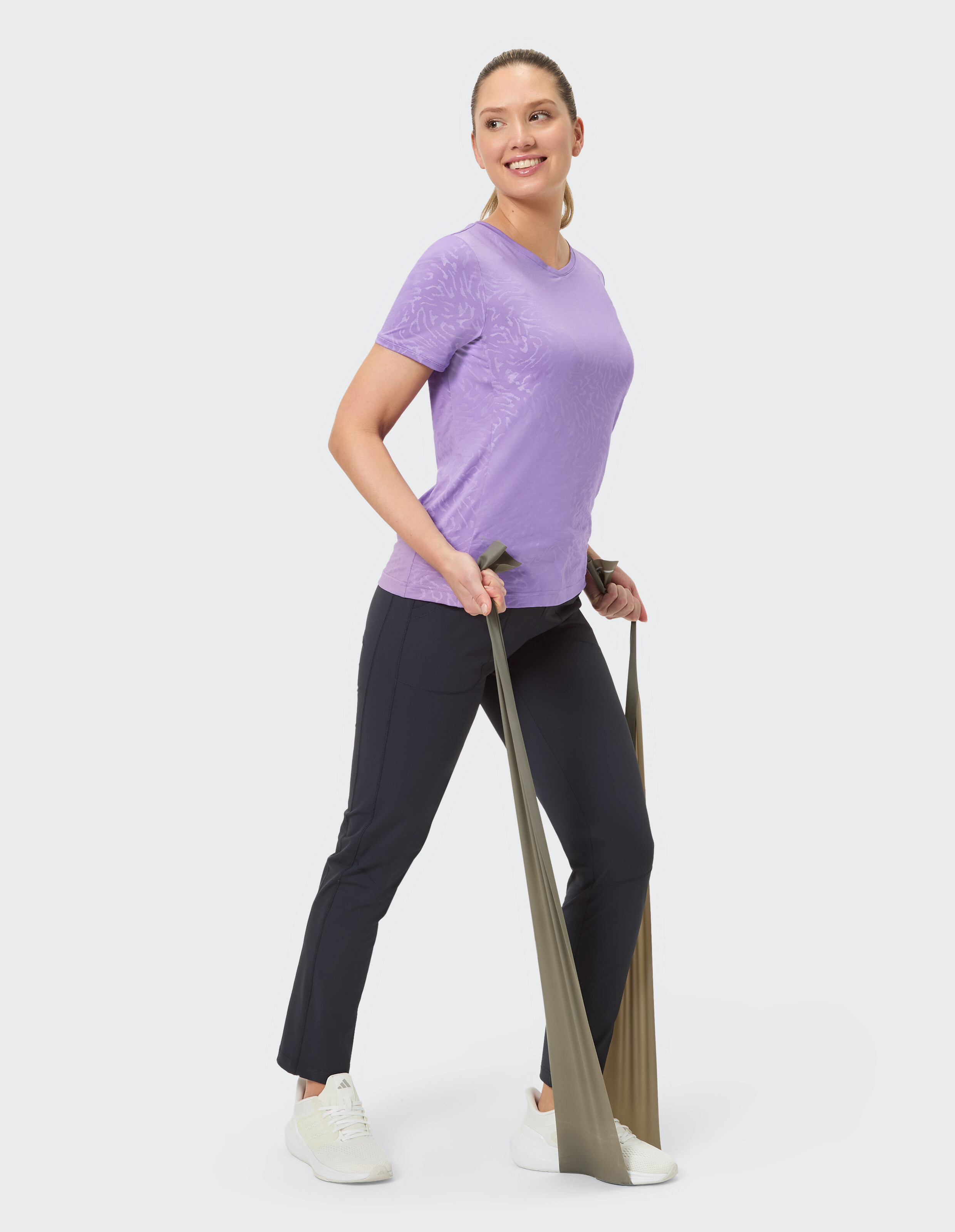 Frau in einem lila T-Shirt und einer schwarzen Hose trainiert mit Widerstandsbändern.