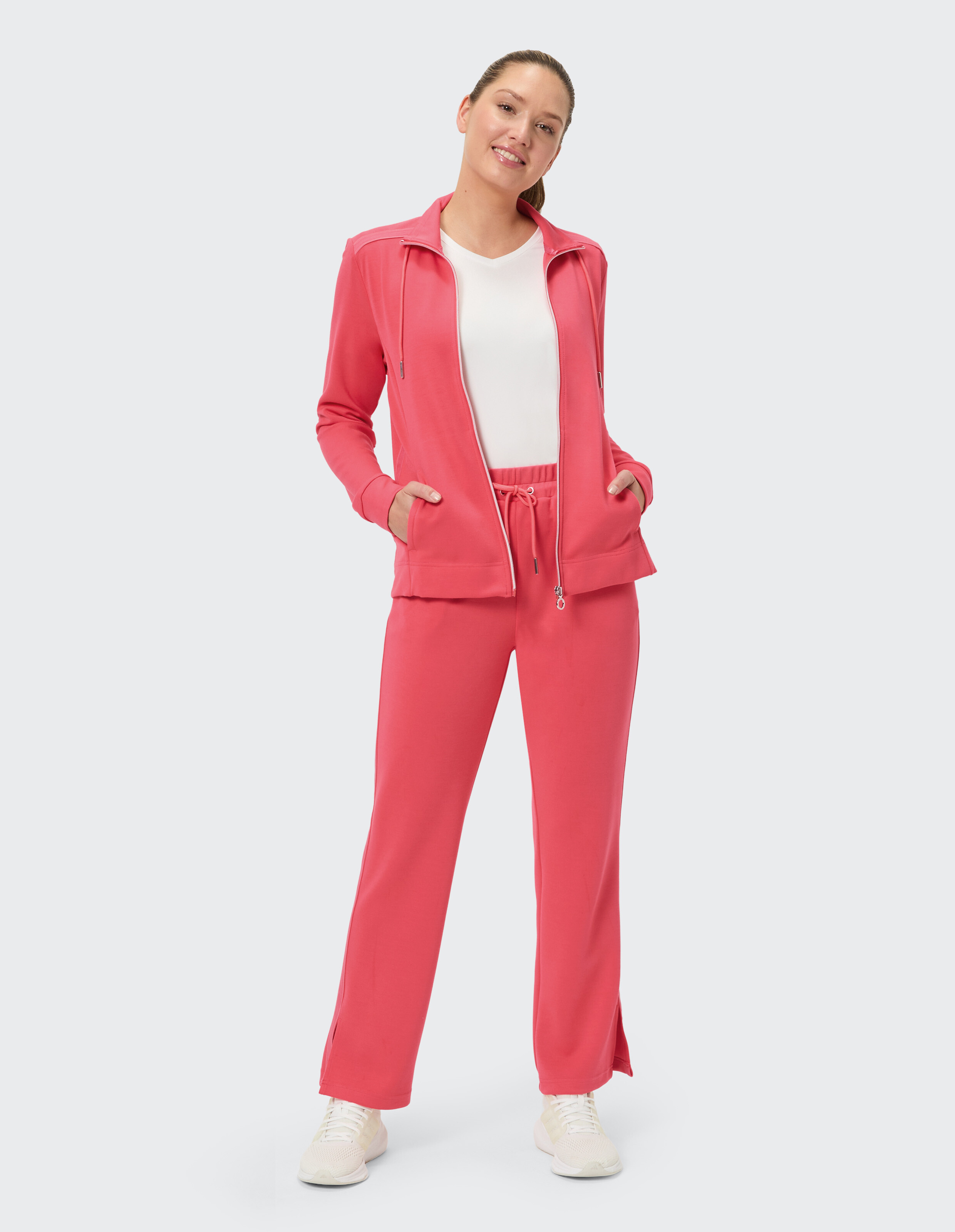 Das Model trägt einen kuscheligen rosafarbenen Trainingsanzug mit einer Jacke mit Reißverschluss und einer Hose mit Kordelzug, perfekt für Freizeitausflüge.