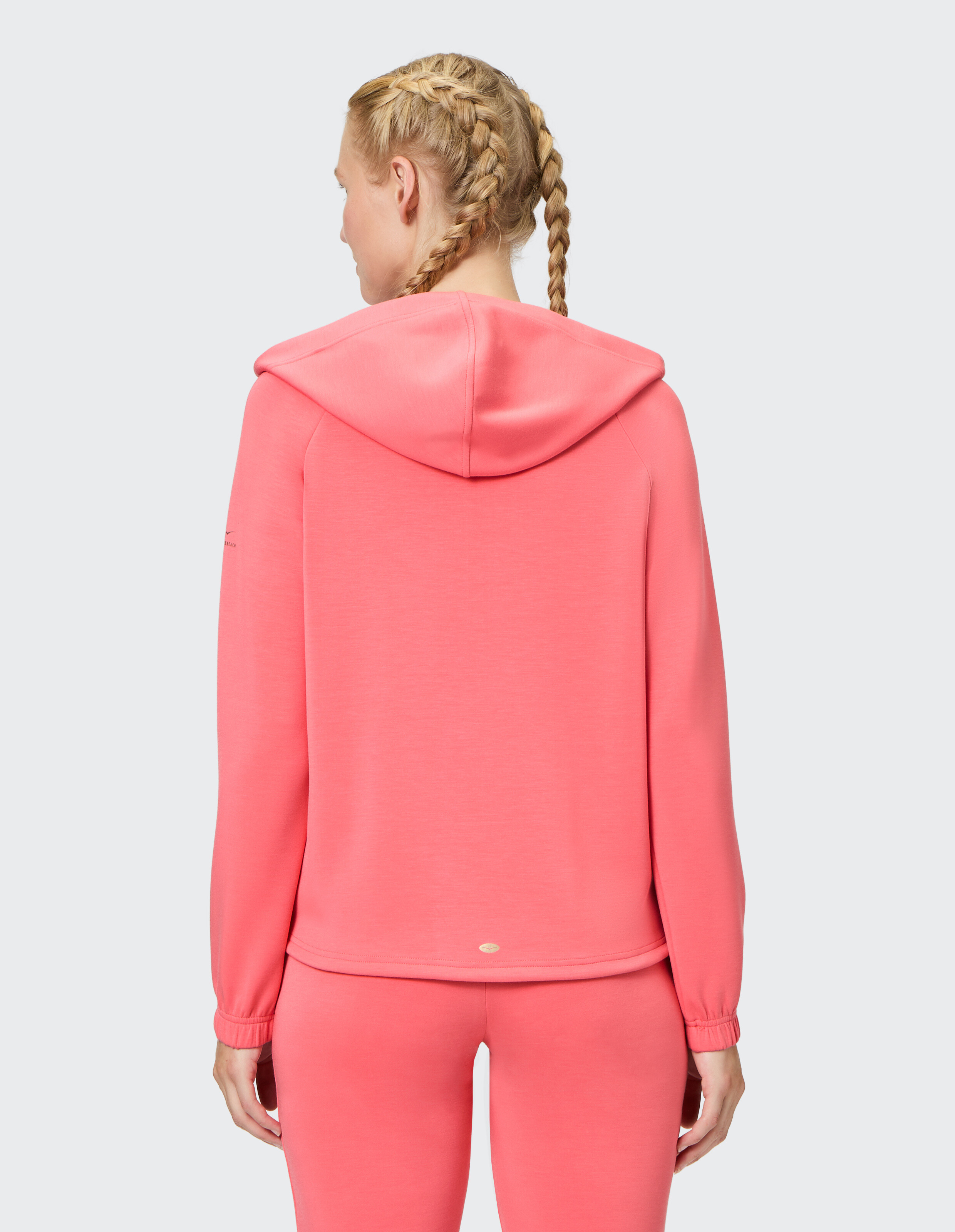 Frau trägt einen kuscheligen korallenrosa Kapuzenpullover, perfekt zum entspannten Faulenzen oder Reisen.