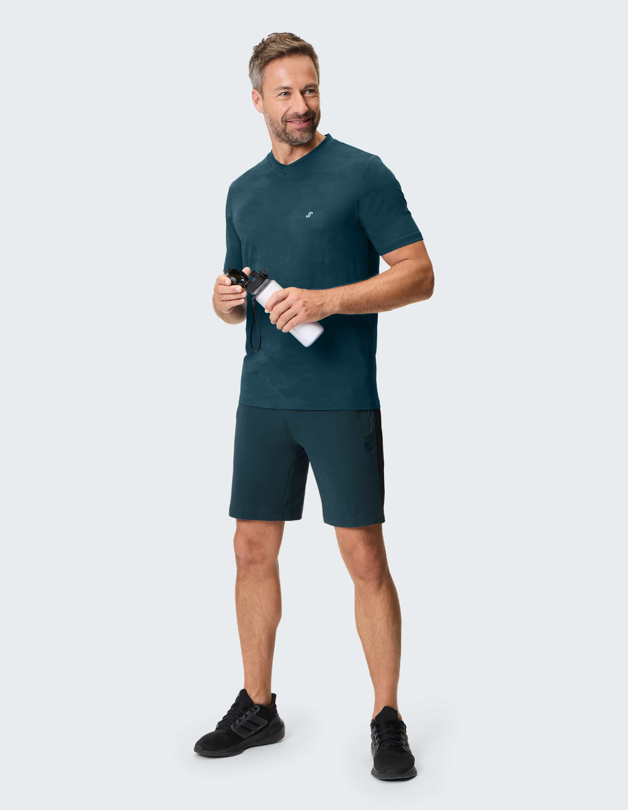 Mann in dunkelblauem T-Shirt und passenden Freizeitshorts mit einer Wasserflasche.