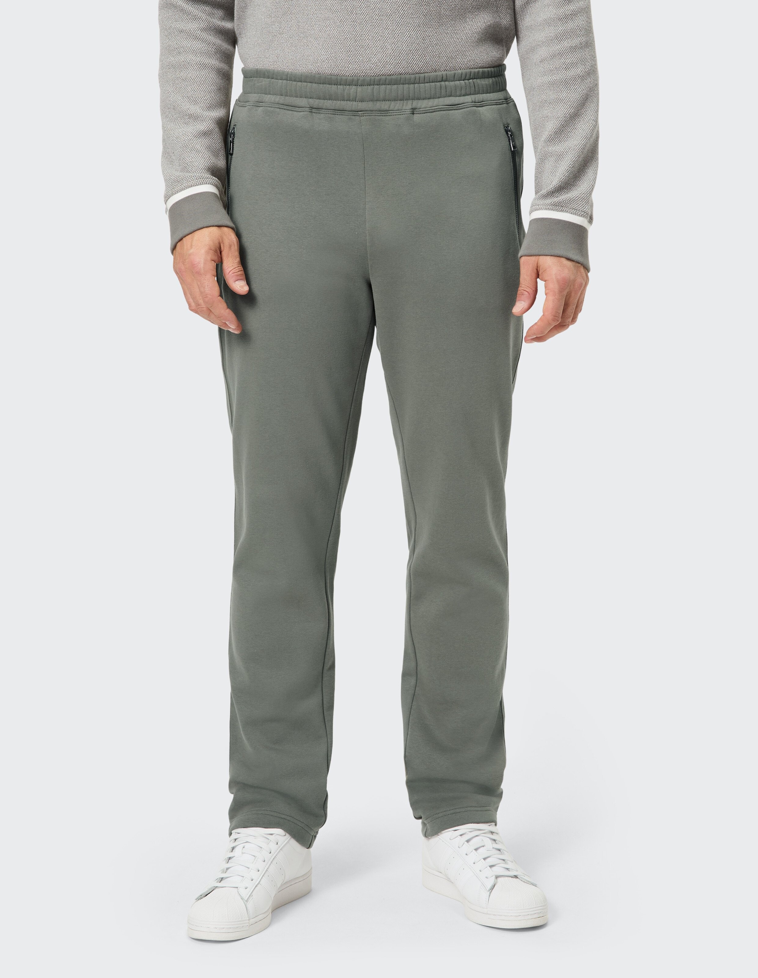 Mann trägt olivgrüne, lässige Jogginghose mit Reißverschlusstaschen für einen bequemen Look.