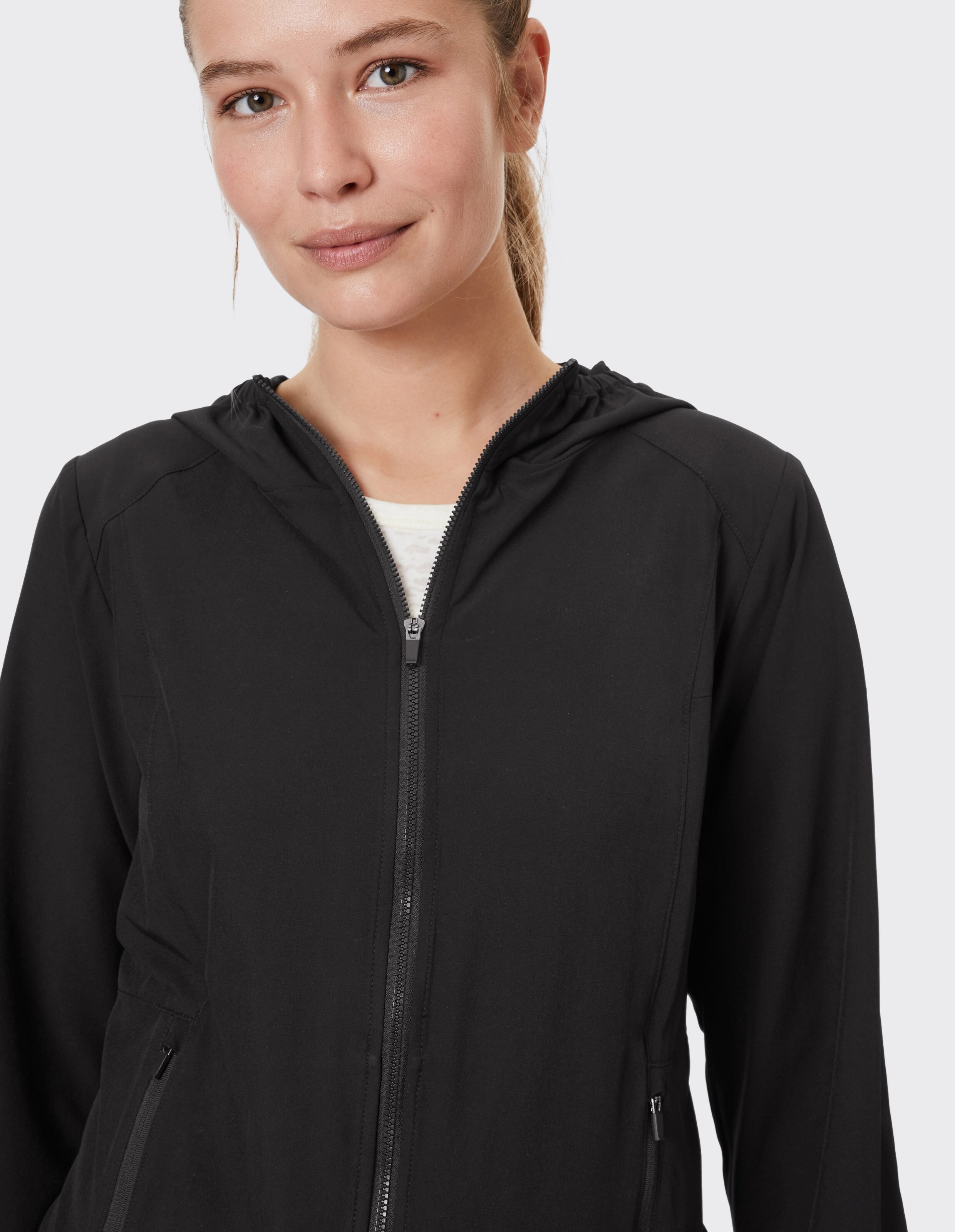Frau trägt eine schwarze Venice Beach Funktionsjacke Hazel mit Kapuze und Reißverschluss.