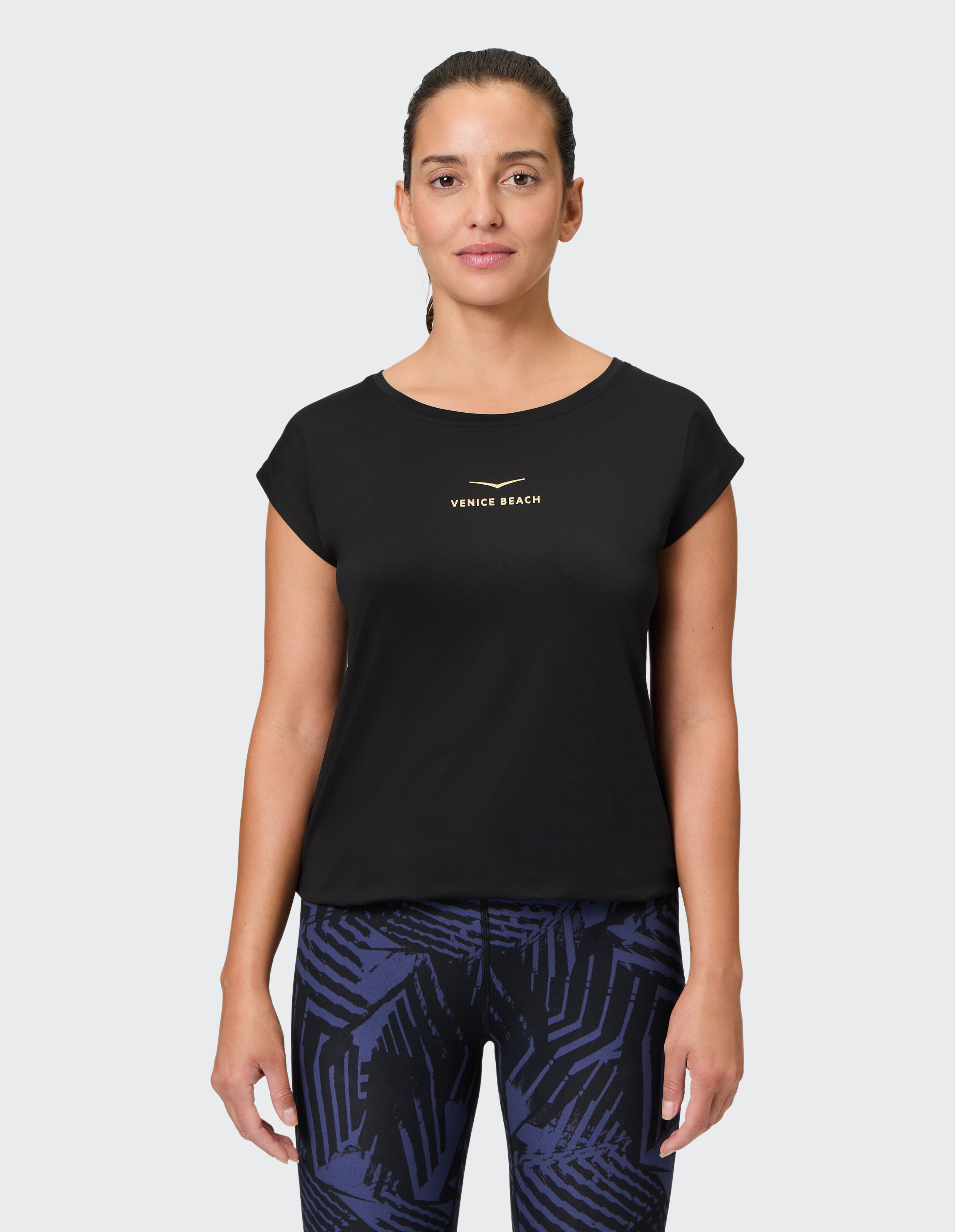 Frau trägt ein schwarzes Venice Beach-T-Shirt und gemusterte Leggings für Freizeitkleidung.