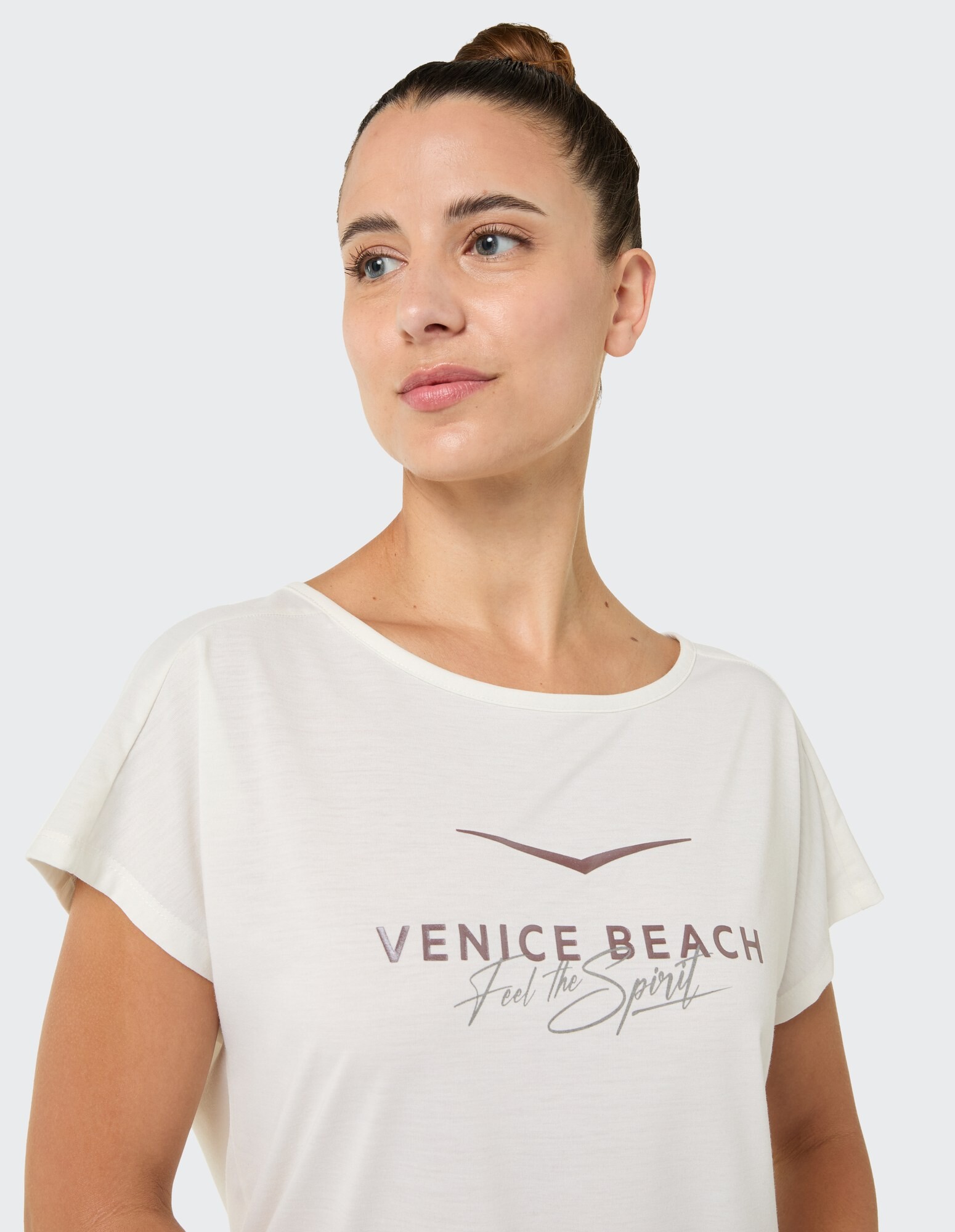 Das Model trägt ein cremefarbenes Venice Beach-Grafik-T-Shirt, perfekt für Freizeitausflüge.