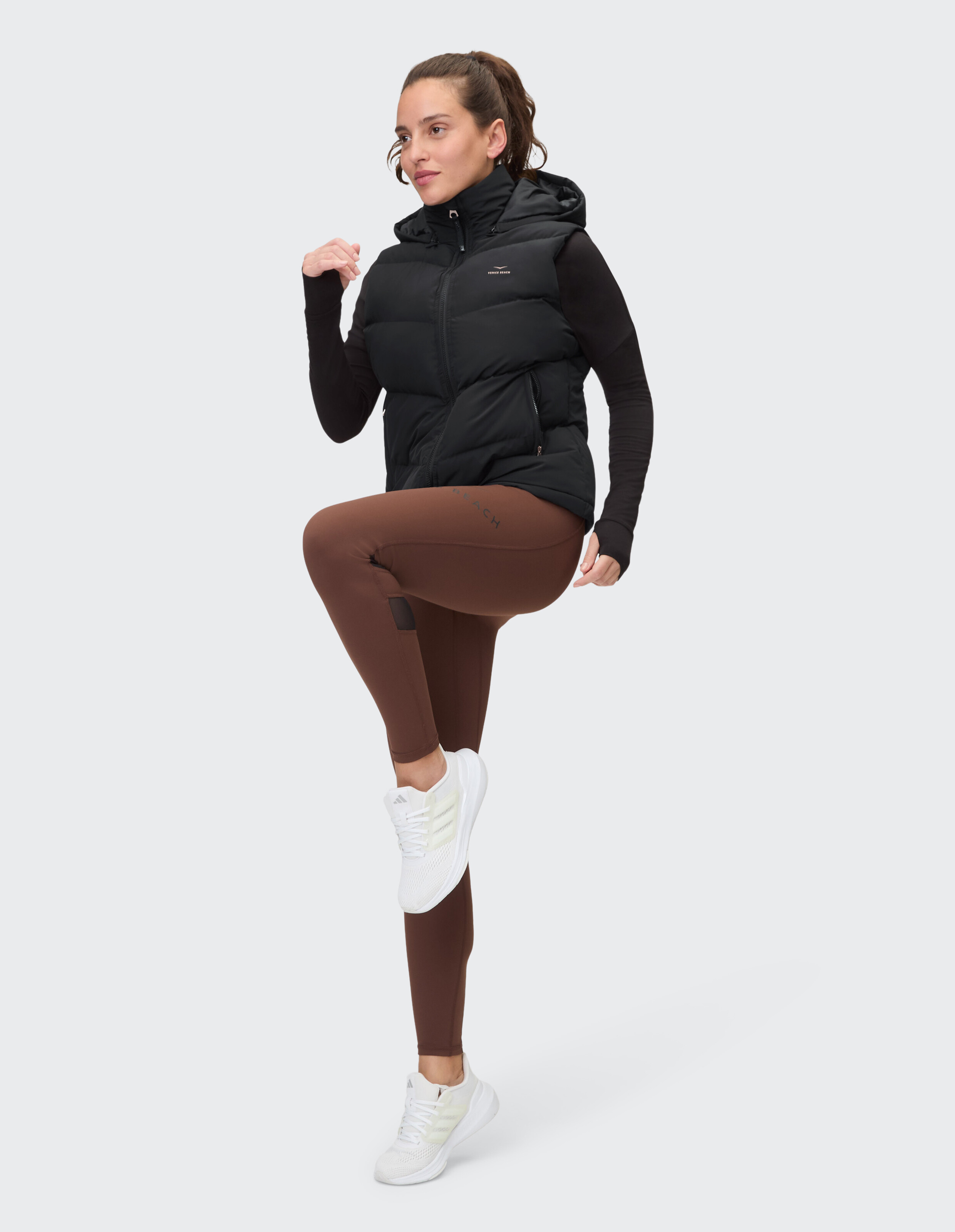 Frau in schwarzer Pufferweste und braunen Leggings, stilvolles, lässiges Activewear-Outfit.