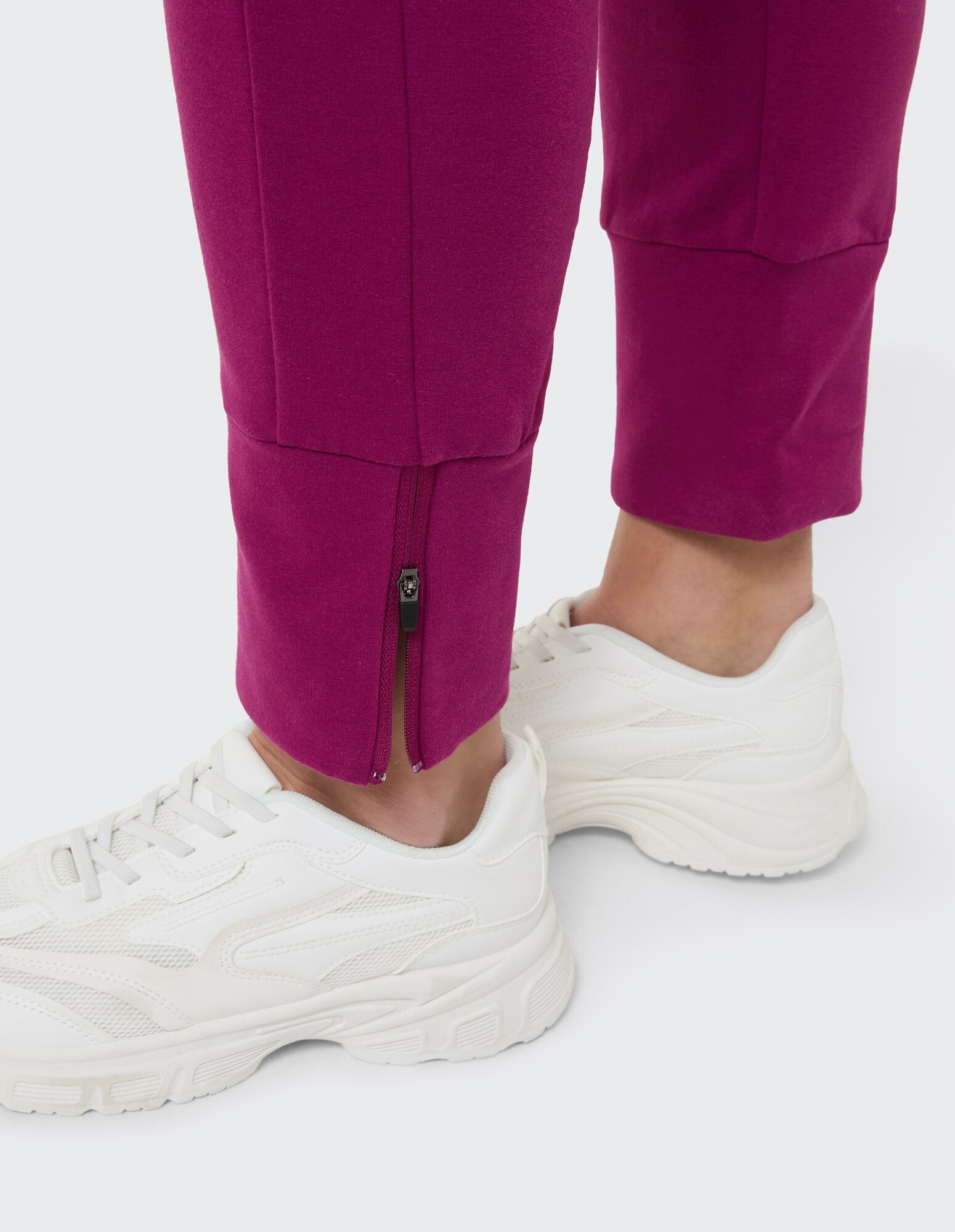 Nahaufnahme einer fuchsiafarbenen Jogginghose mit Reißverschlussbündchen und weißen Turnschuhen.