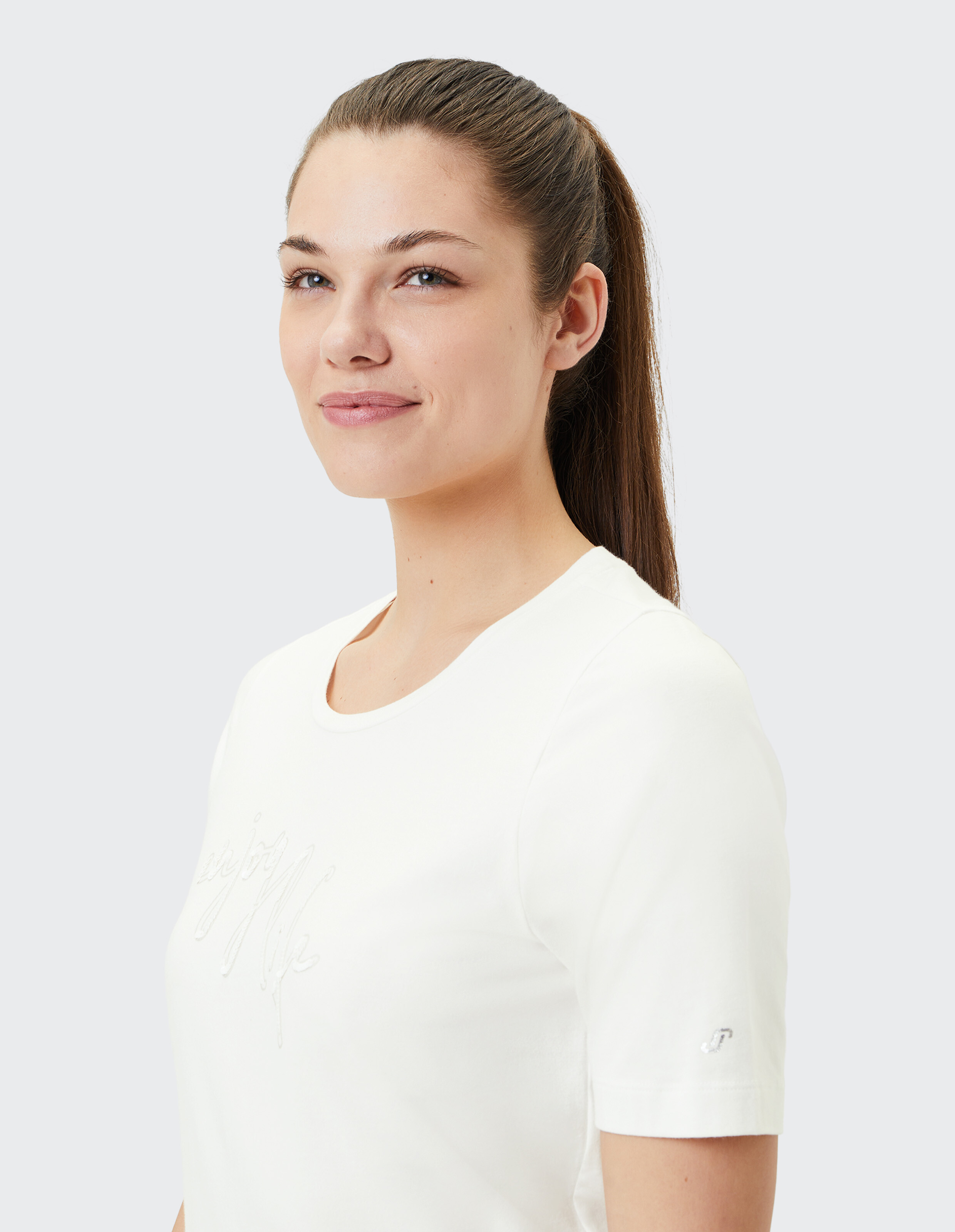 Frau trägt ein weißes, lässiges T-Shirt mit kurzen Ärmeln und gestickten Details.