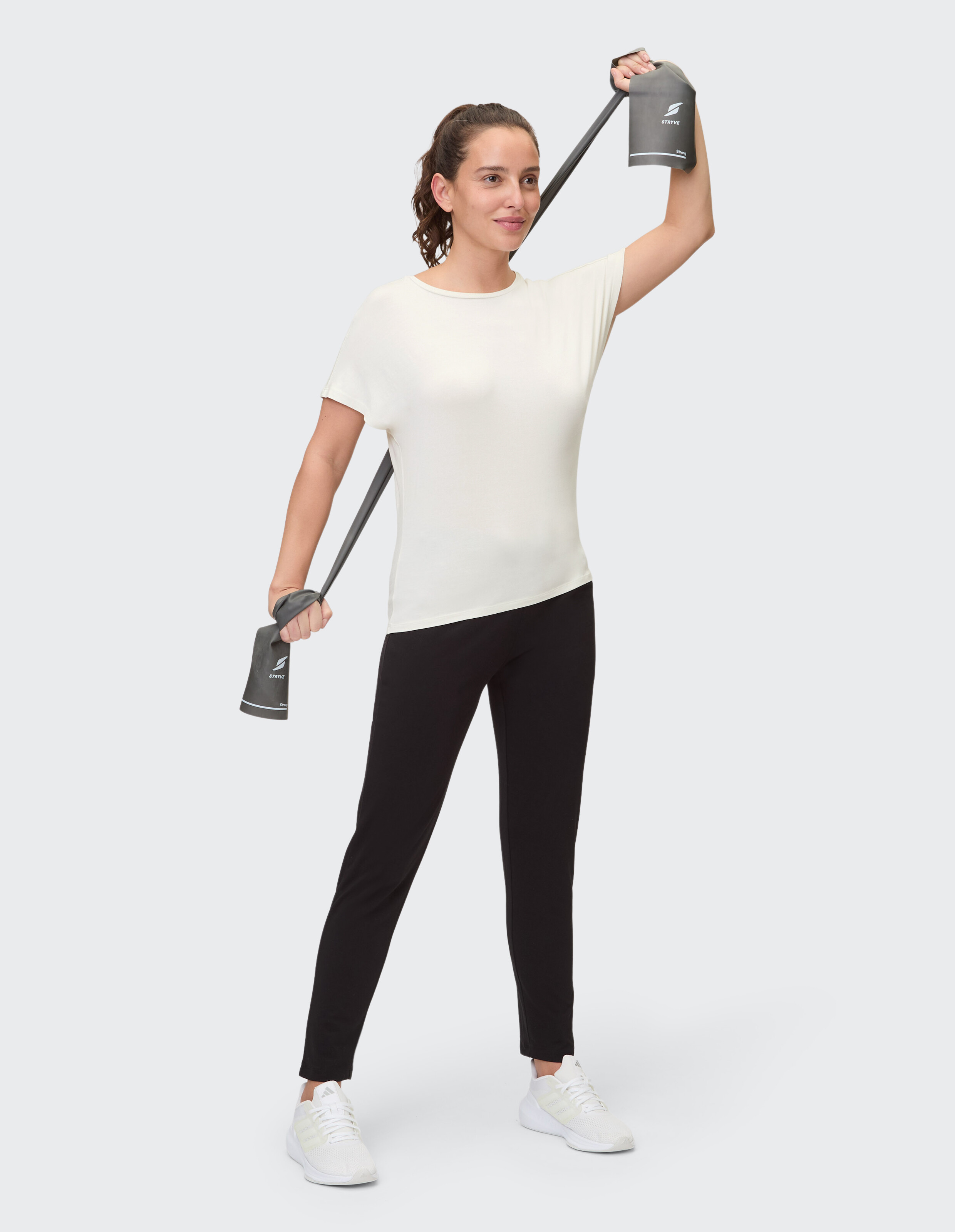Frau in einem hellcremefarbenen Top und schwarzen Leggings trainiert mit einem Widerstandsband.