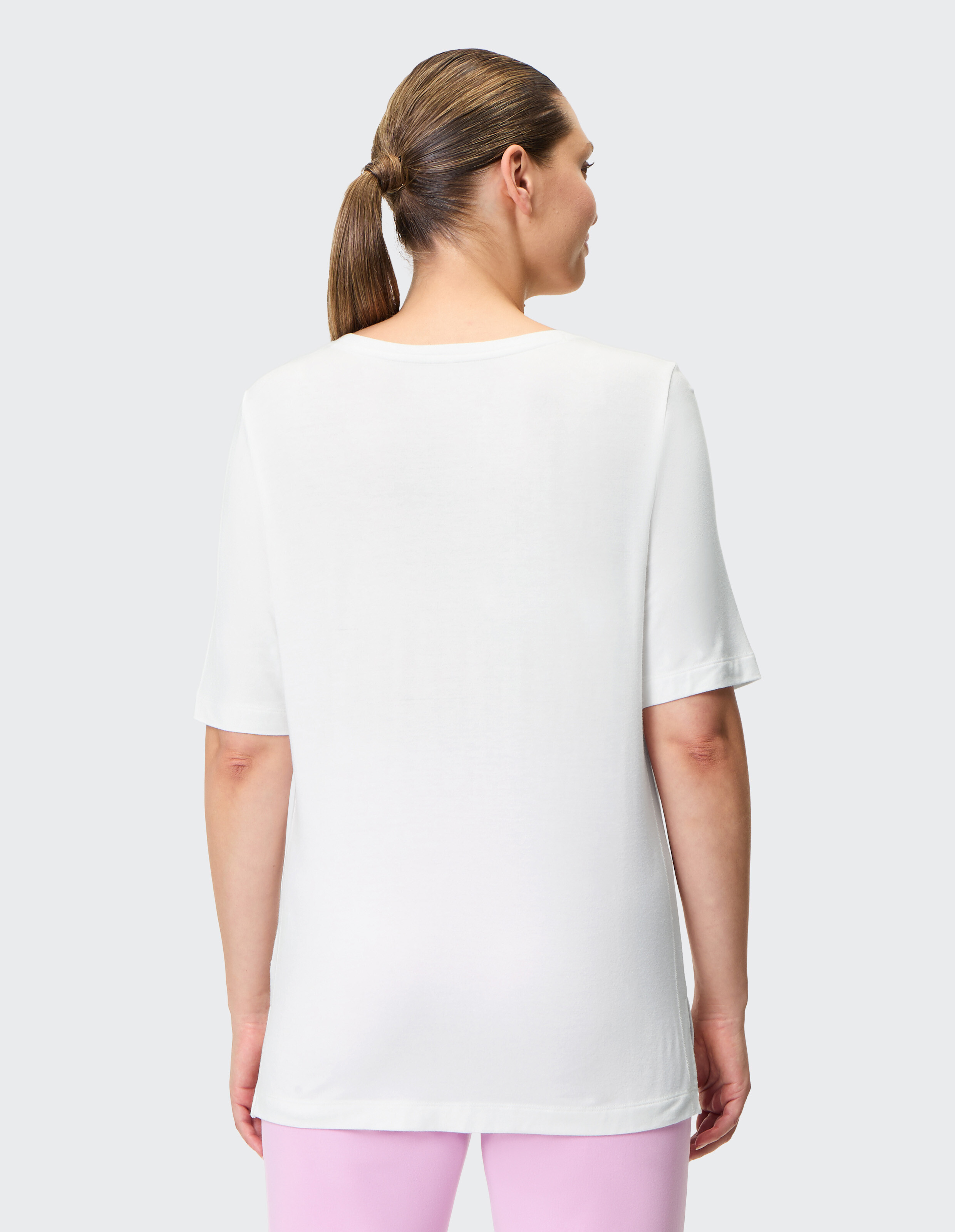 Rückansicht einer Frau in einem weißen Freizeit-T-Shirt gepaart mit einer rosa Hose.