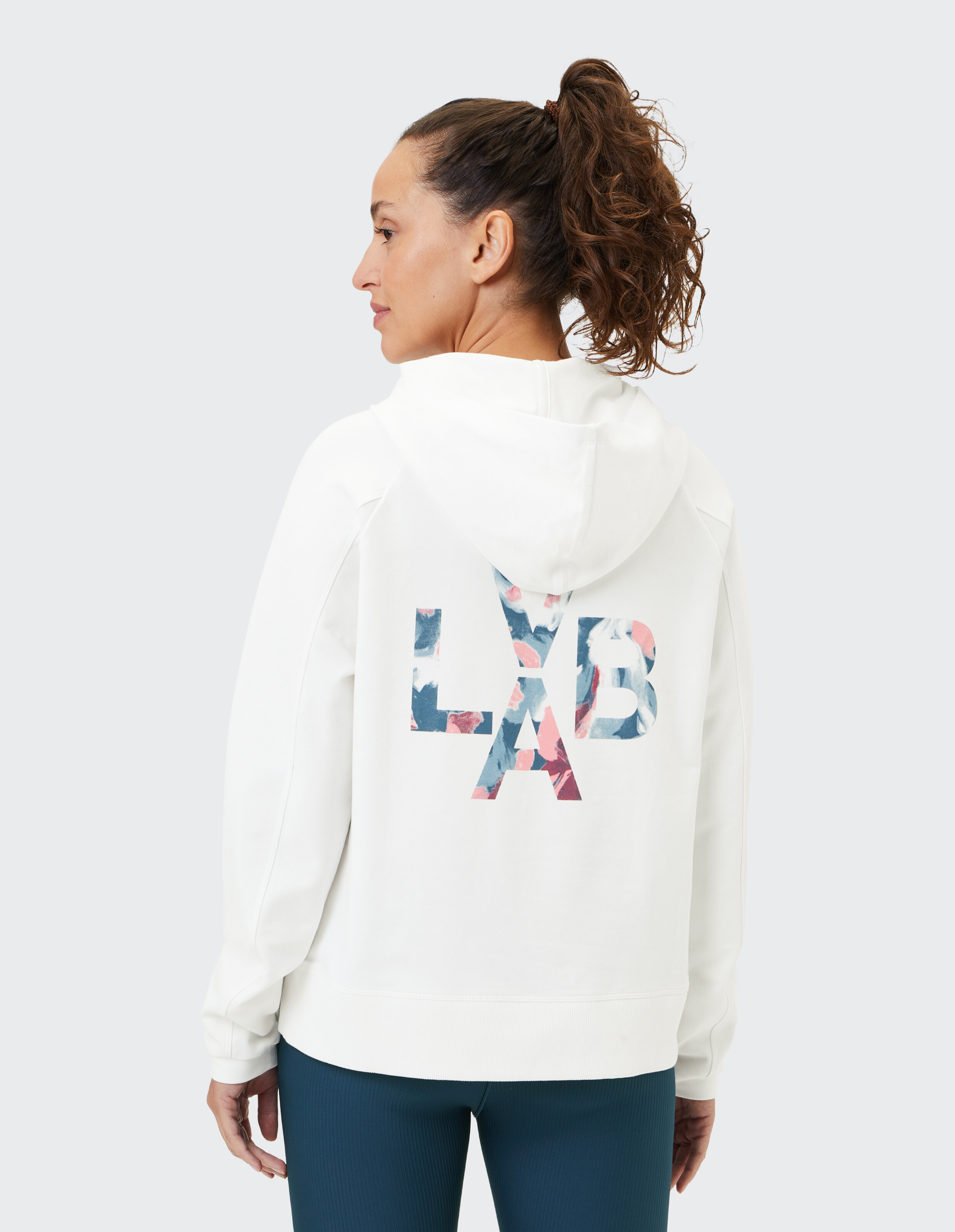 Frau trägt einen weißen ELBSAND-Hoodie mit floralem Logo-Print auf der Rückseite.