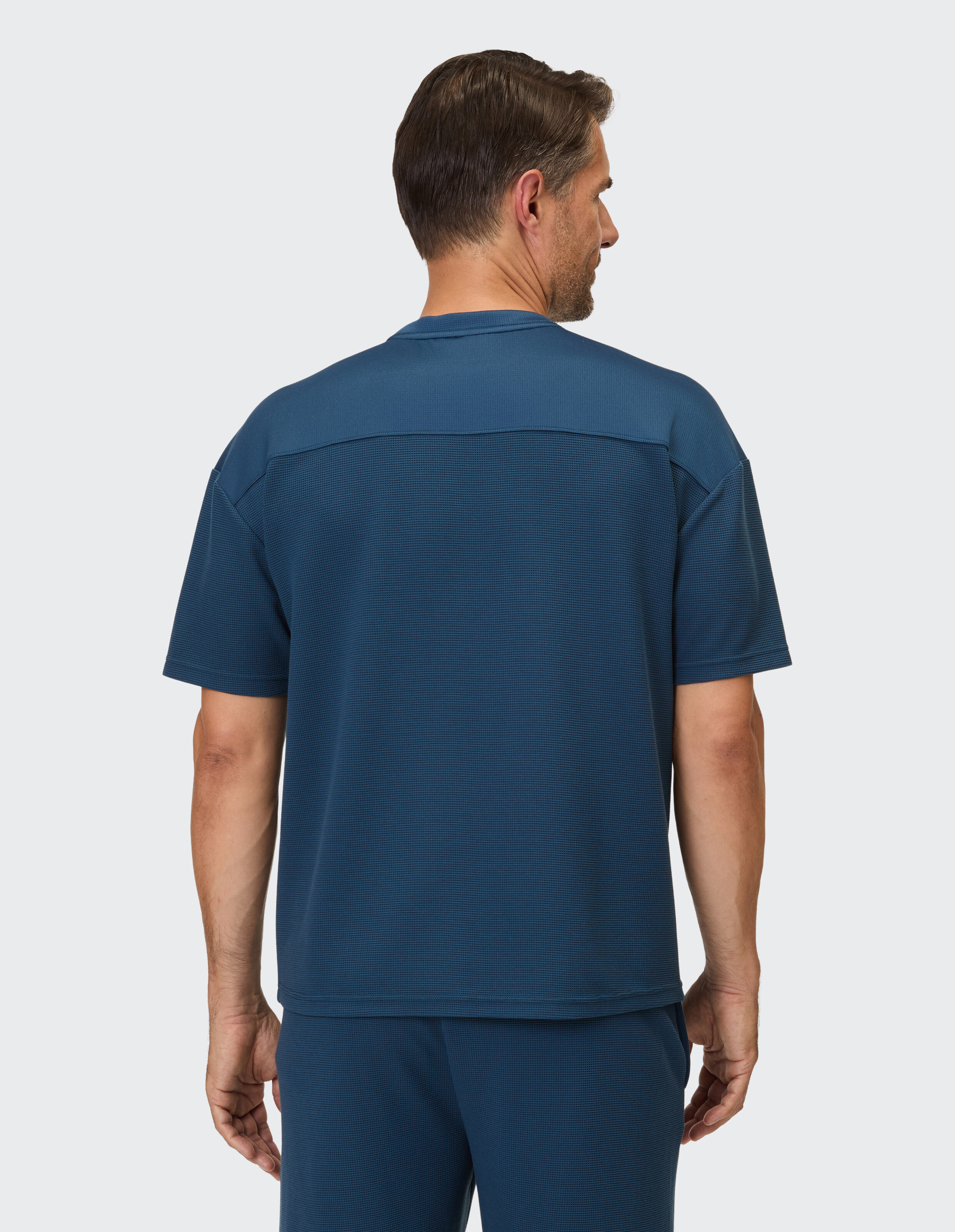 Ein Mann trägt eine blaue, kurzärmelige Hemdbluse mit strukturiertem Muster.