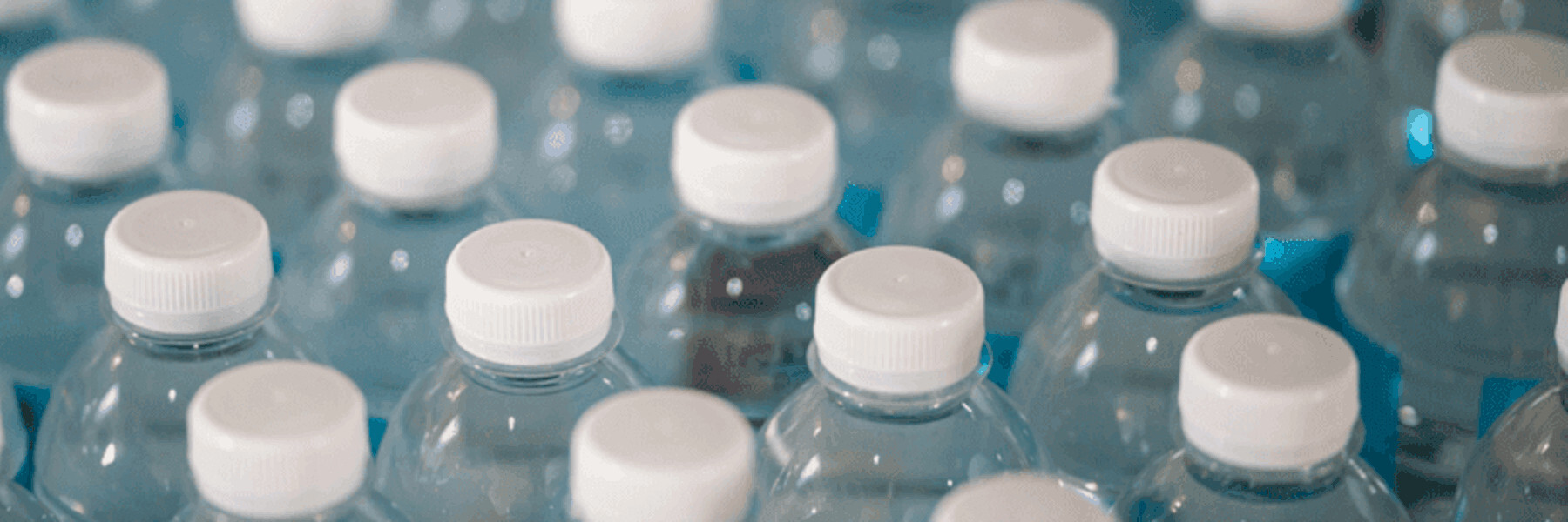 Nahaufnahme von Wasserflaschen mit weißen Verschlüssen, ordentlich angeordnet auf einer blauen Oberfläche.