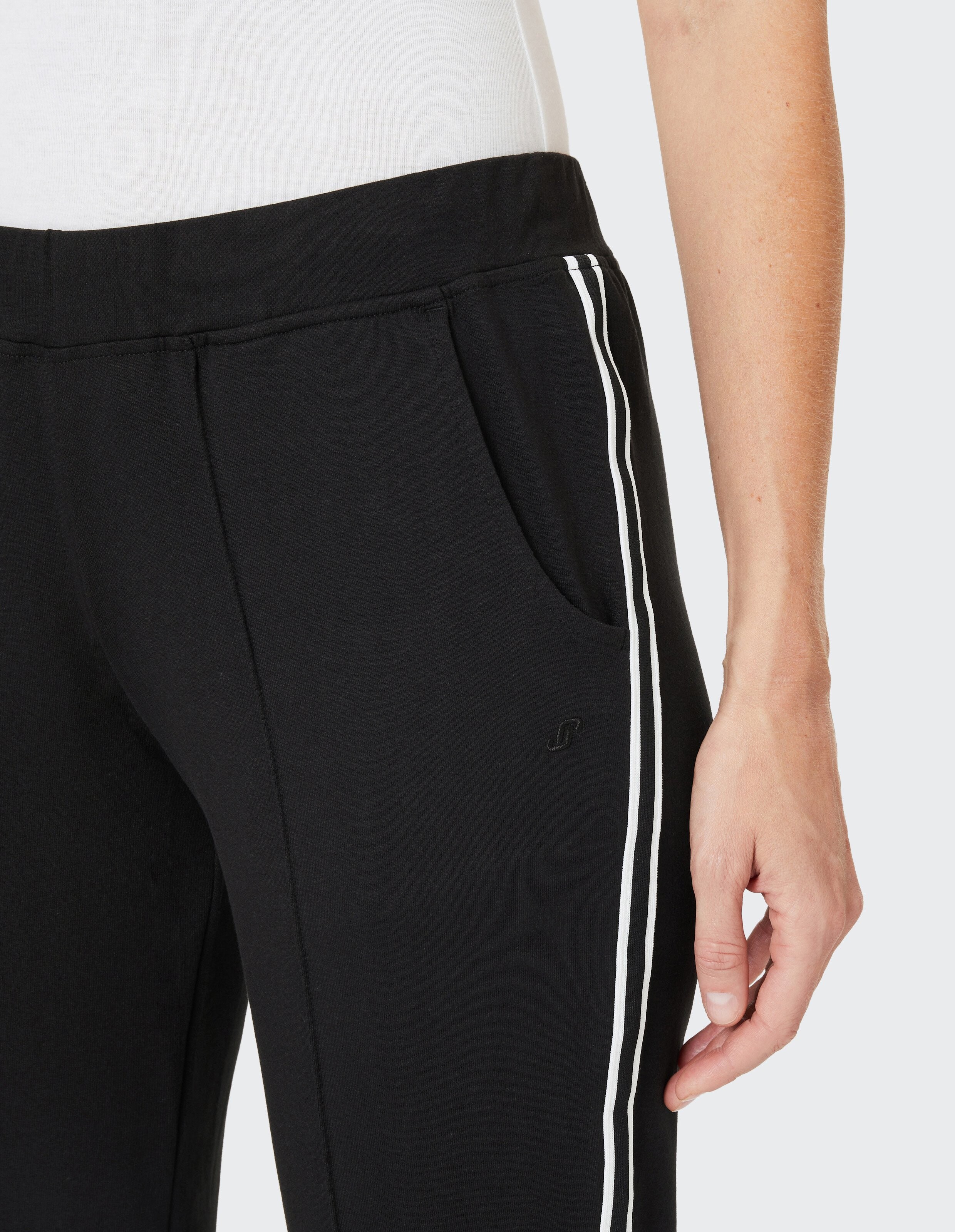 Schwarze Jogginghose mit weißem Streifen entlang der Seitennaht, eine Hand in der Hosentasche, auf hellem Hintergrund.