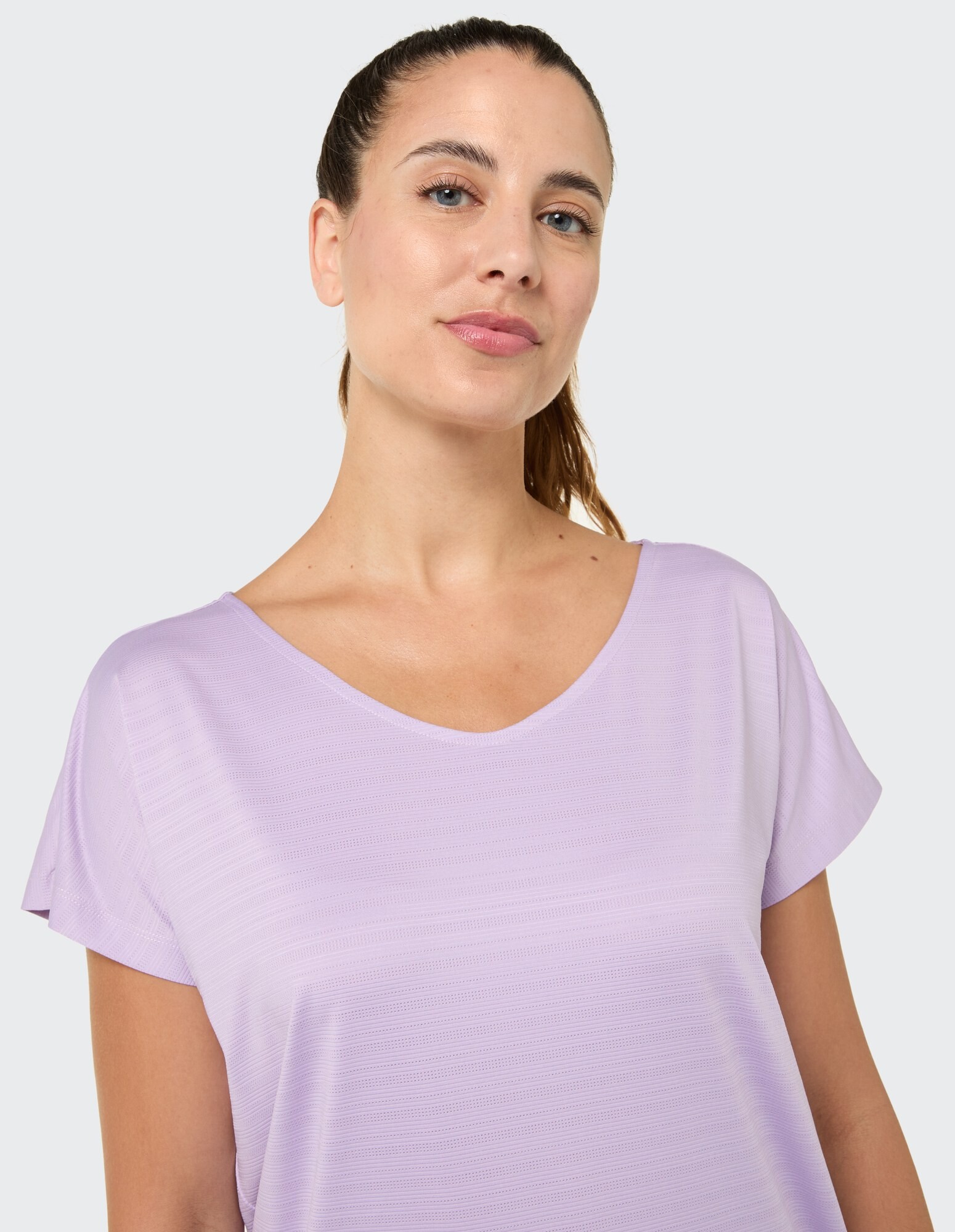 Das Model trägt ein hellviolettes Freizeitoberteil mit lockerer Passform und kurzen Ärmeln.
