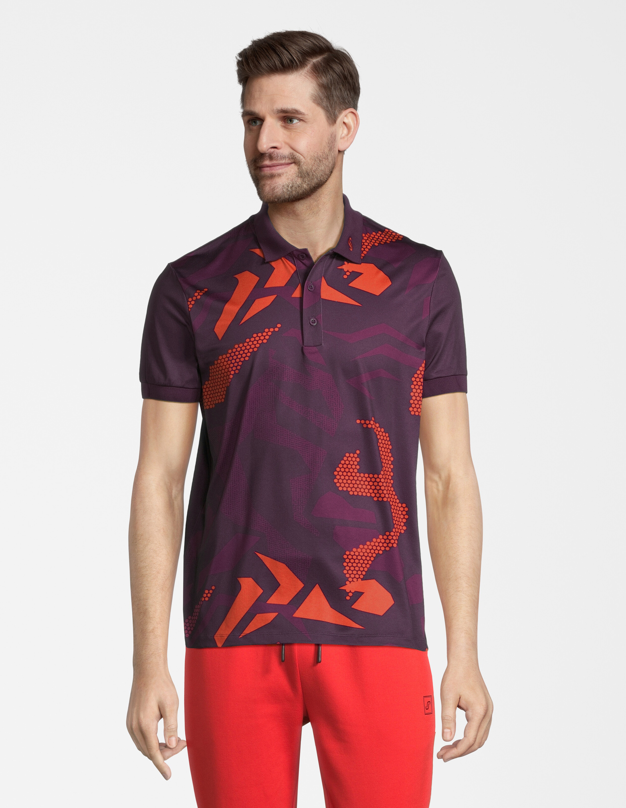 Mann trägt ein lila Poloshirt mit orangefarbenen geometrischen Mustern und eine rote Freizeithose.