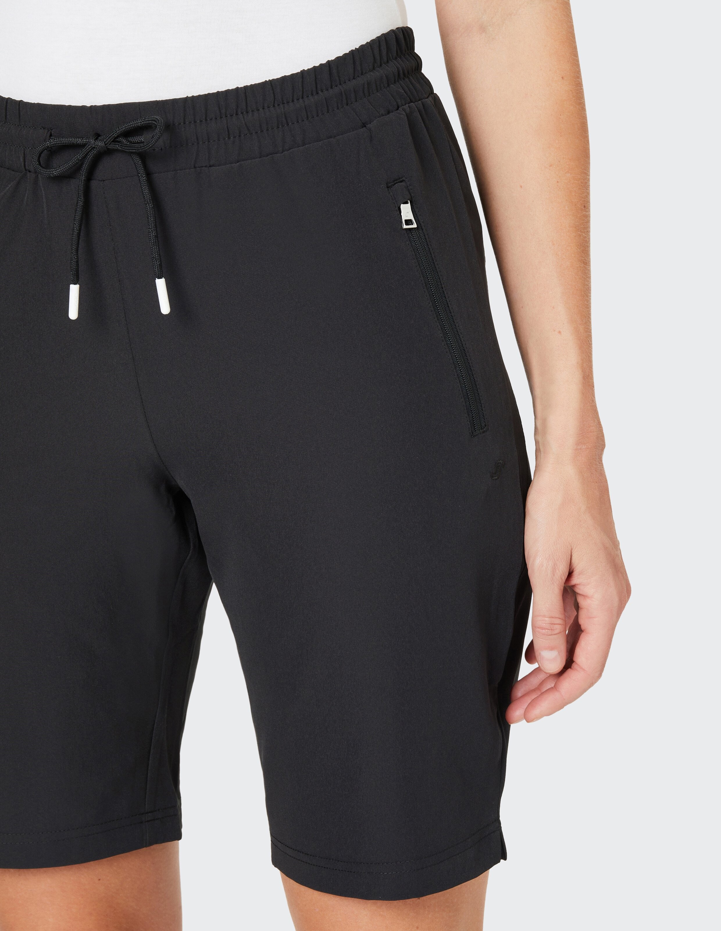 Schwarze Shorts mit Kordelzug und Reißverschlusstasche, getragen von einer Person mit weißem Oberteil, Detailansicht.
